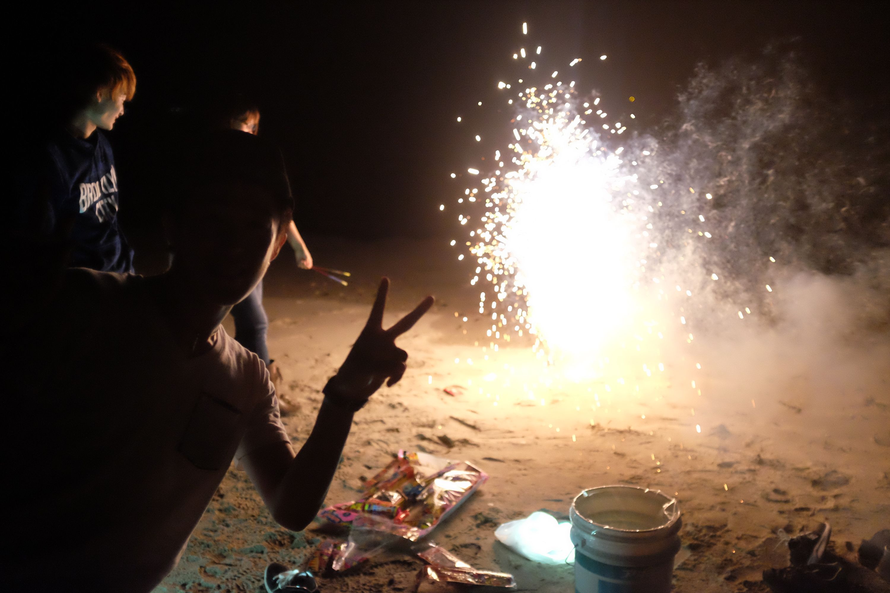 Three young people light fireworks on the beach.