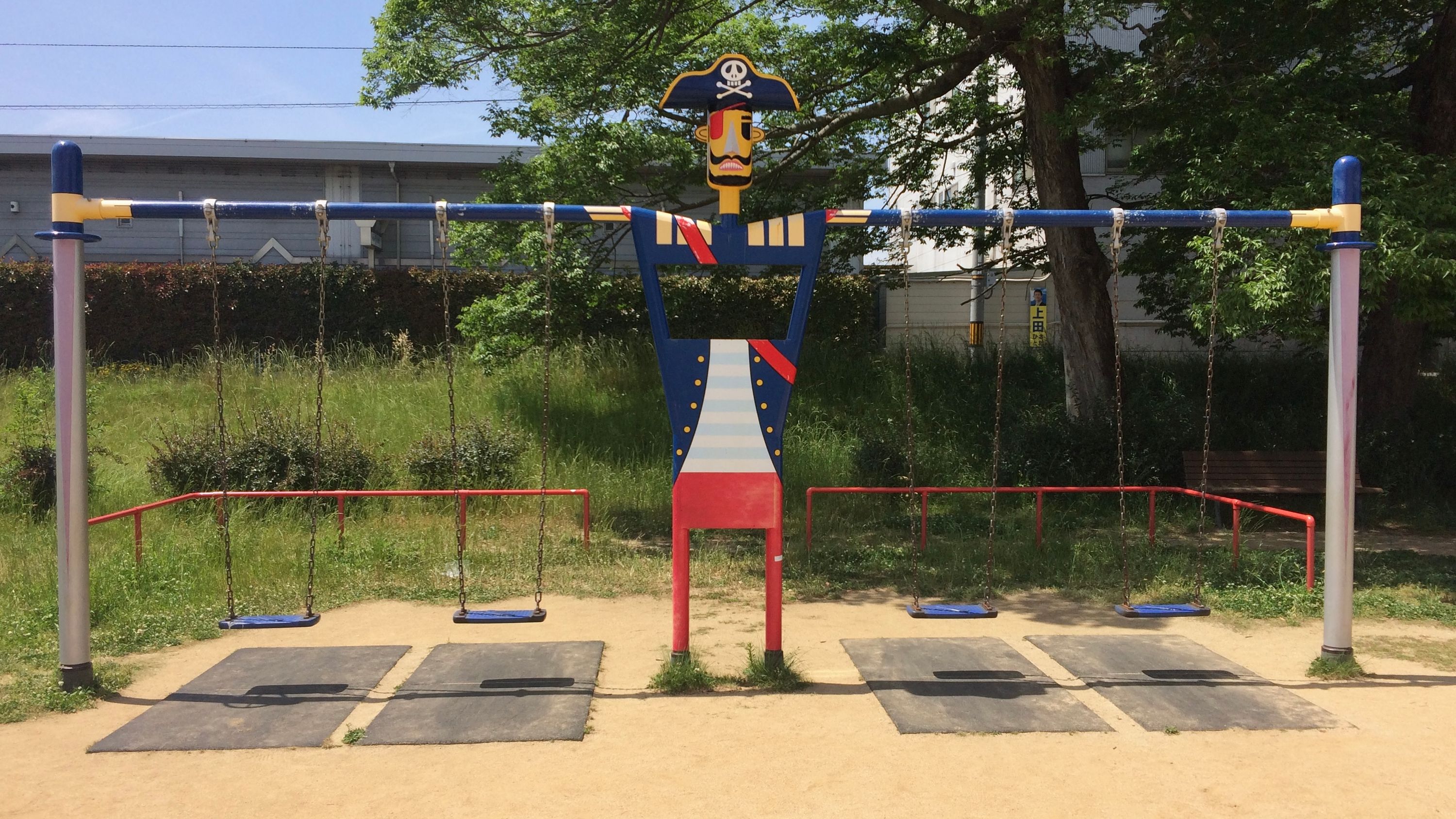 A figure of a pirate with very long arms holds four swings at a playground.