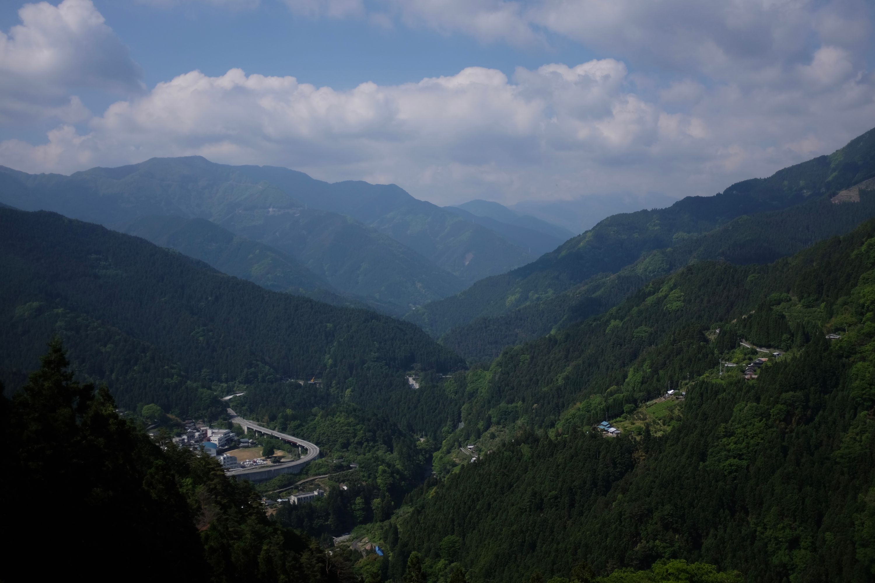 Panorama of a valley flanked on both sides by forested hillsides, with a road visible in the bottom left.