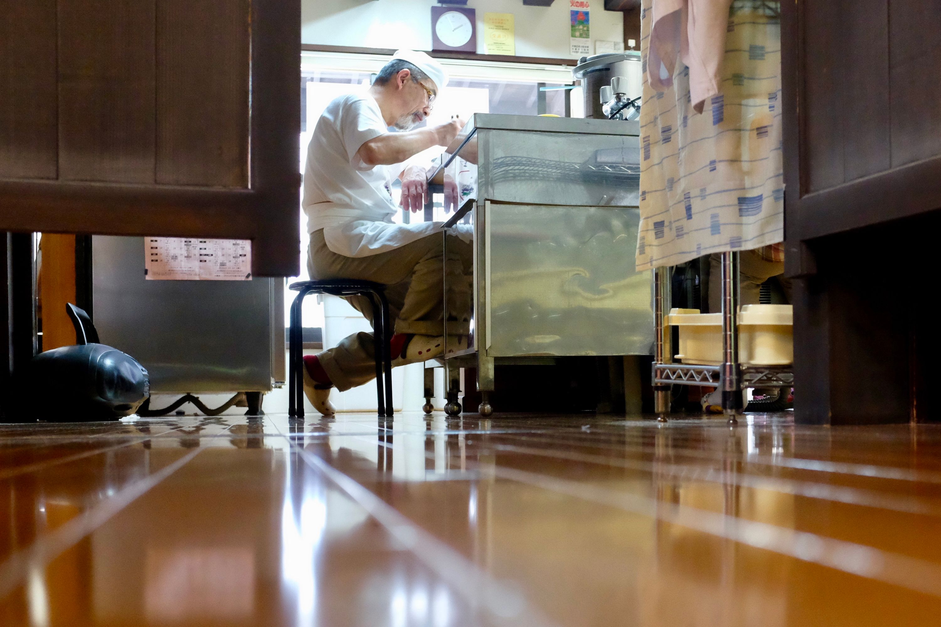 Photographed from a distance, a Japanese chef eats noodles at the kitchen counter of a restaurant.