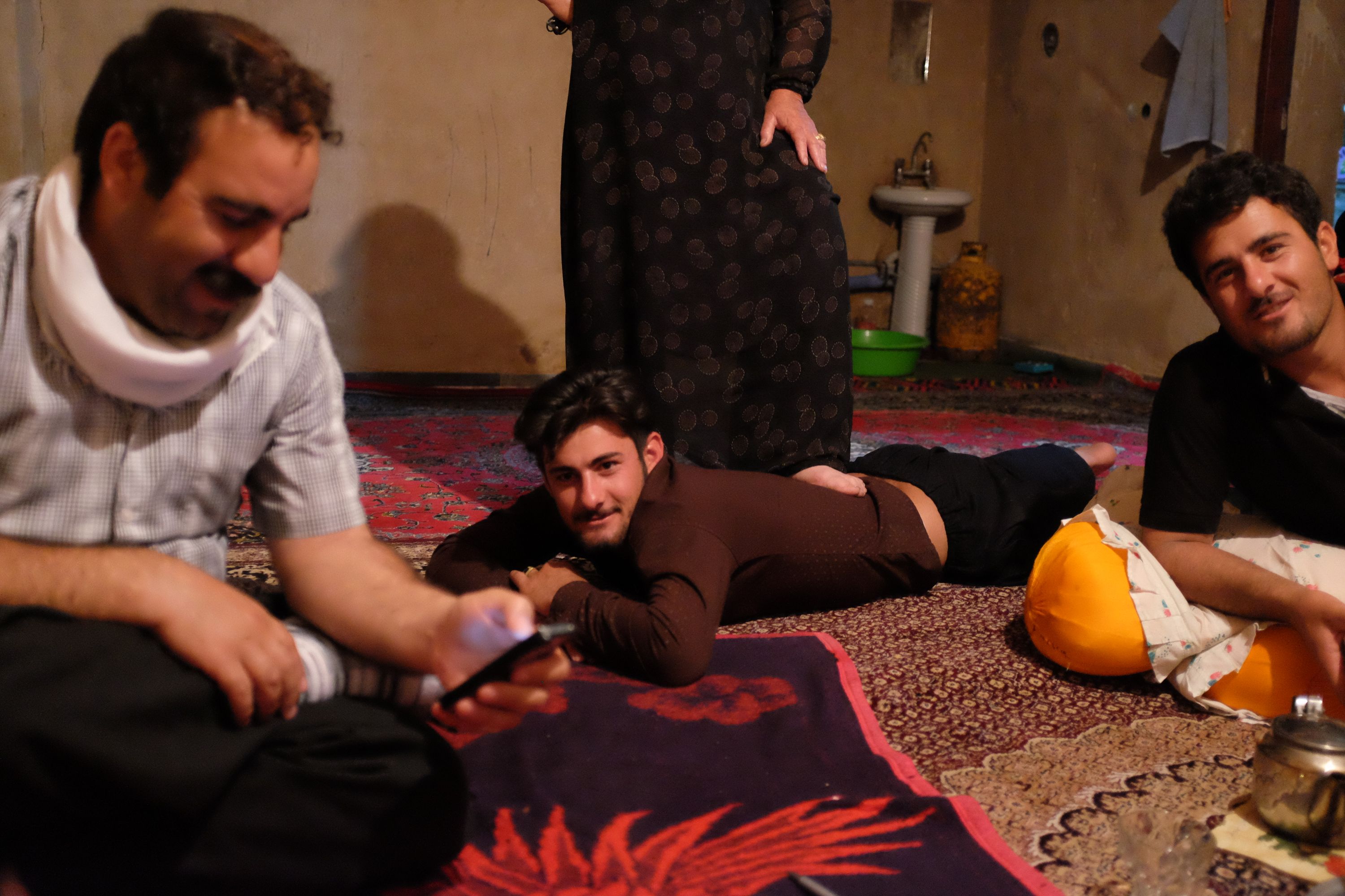 Three young man lie and sit around on a carpeted floor, with a woman stepping lightly on the back of one of them.
