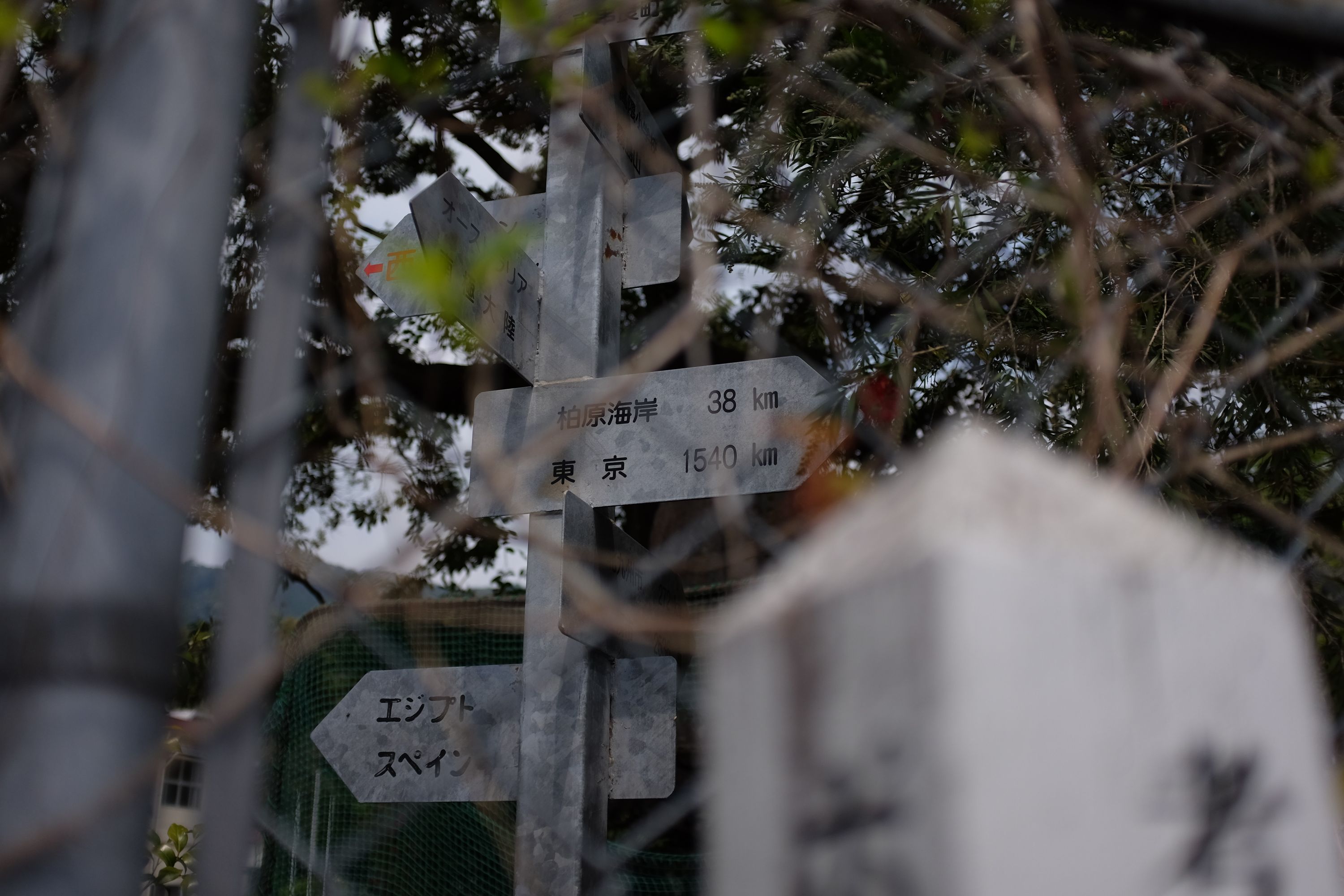 A sign behind a fence shows the distance to the nearest town, and also to Tokyo, 1540 kilometers away.