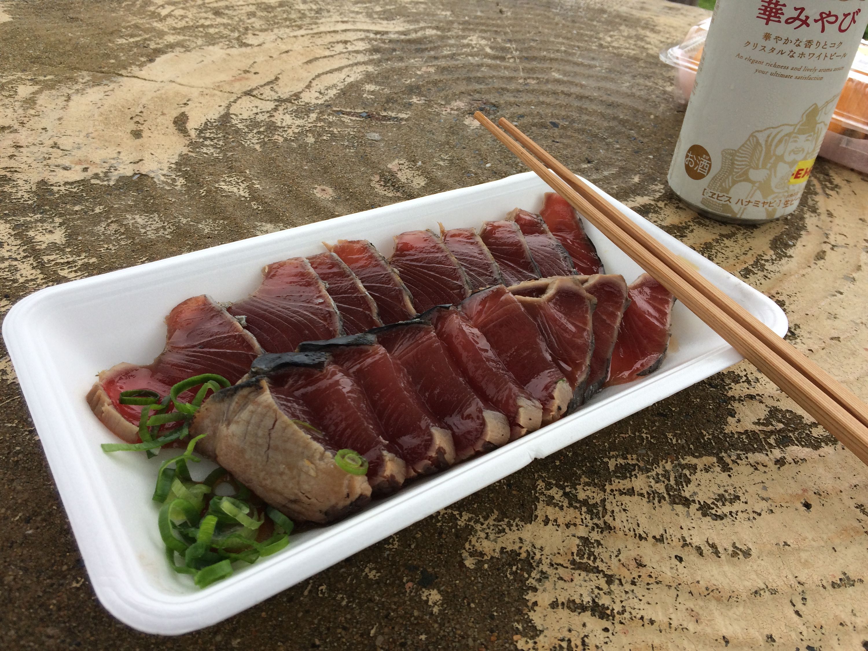 A plate of raw skipjack tuna and a can of beer on an outside table.