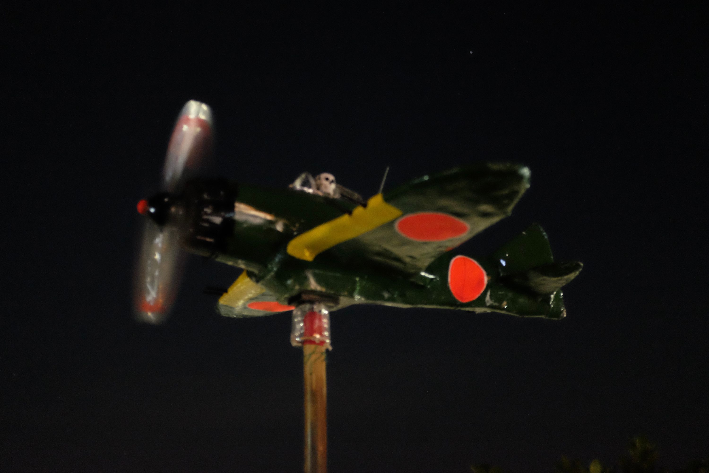 The model of a World War II-era Mitsubishi Zero fighter plane appears to fly across the night sky.