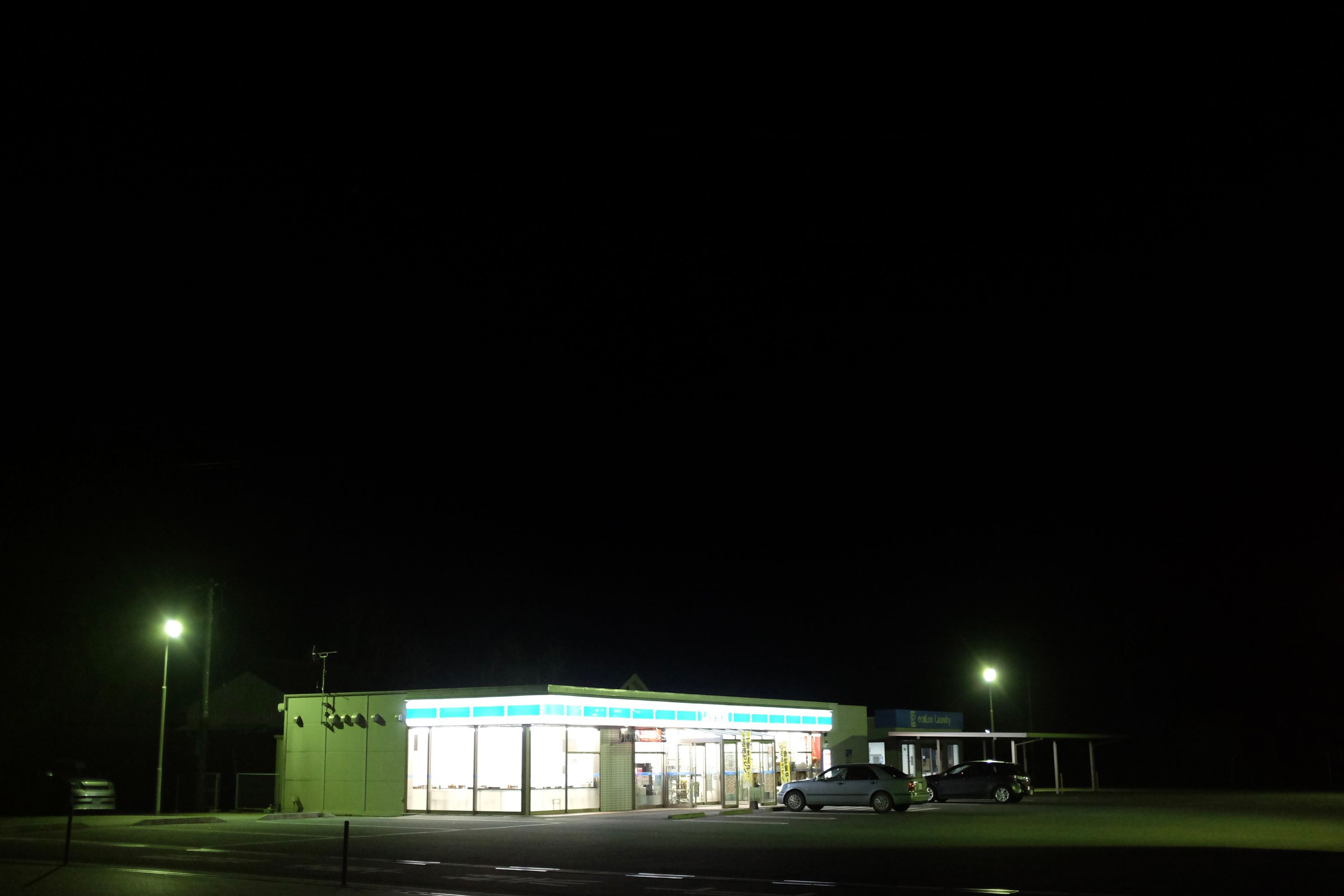 A Lawson convenience store on a pitch black evening, lit up and seen from across its parking lot.