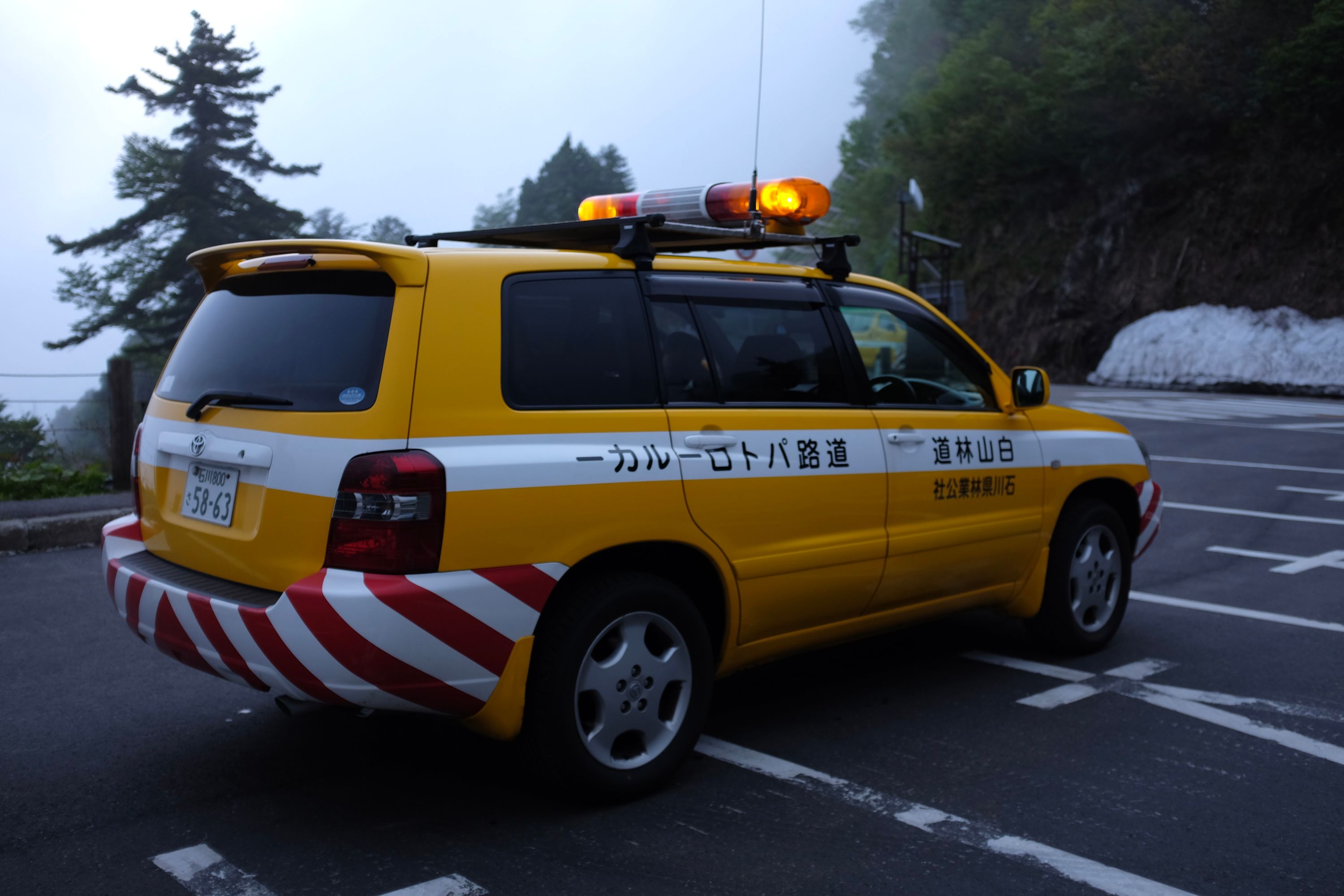 The Toyota utility vehicle, yellow and equipped with light bars, parked on a road with heaps of snow in the background.