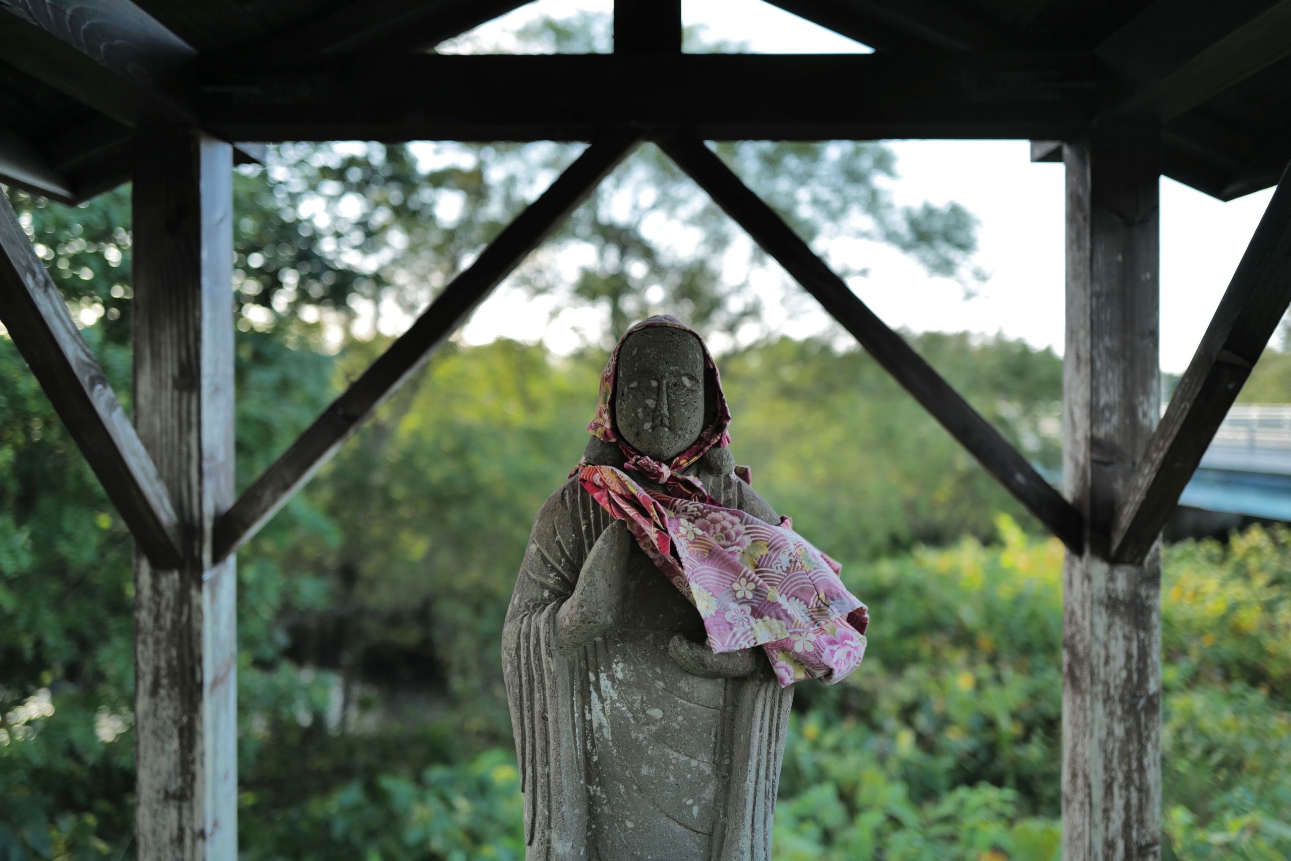 A small statue of a roadside guardian wears a scarf around her neck