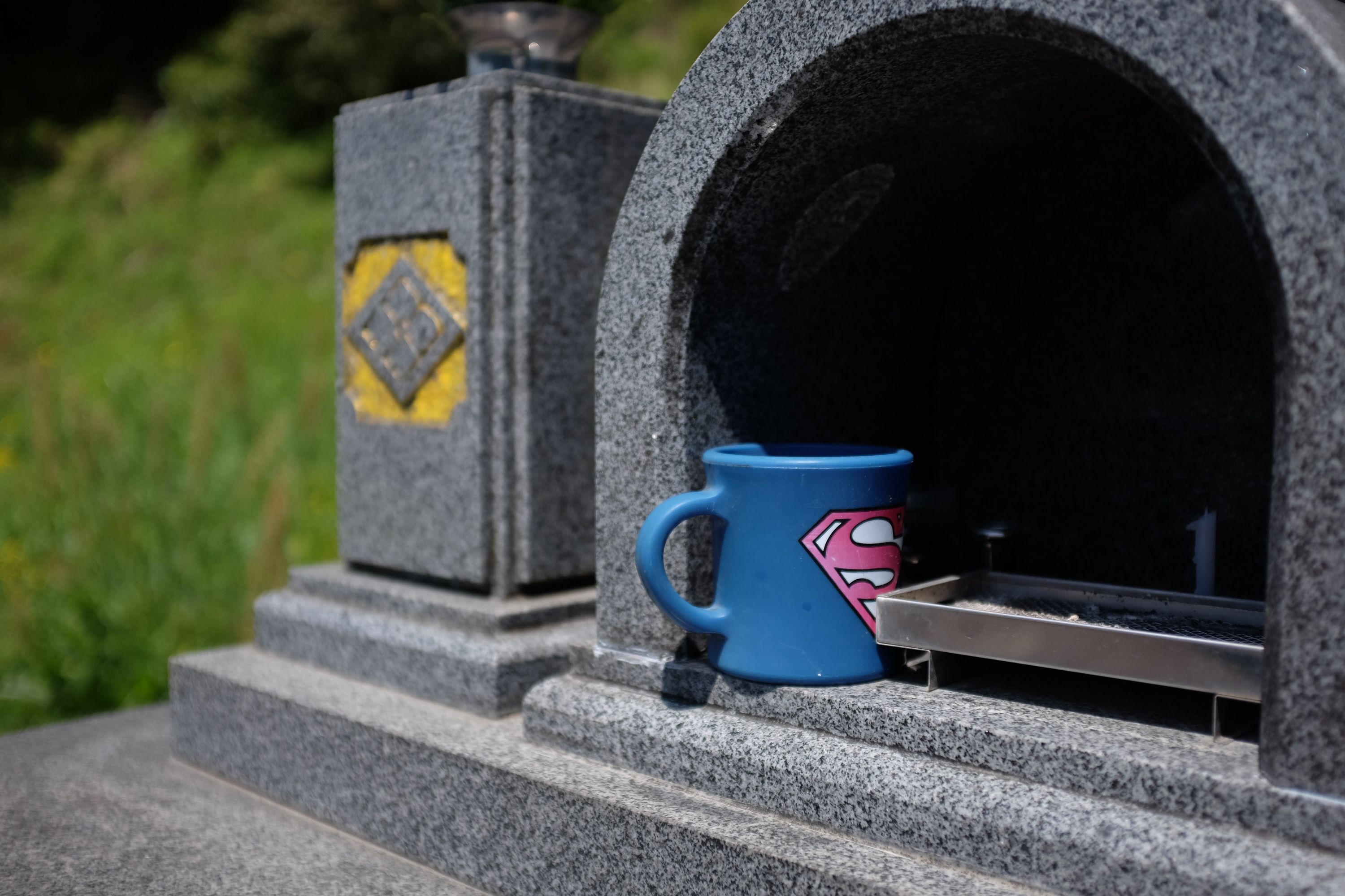 A blue Superman mug on a grave.