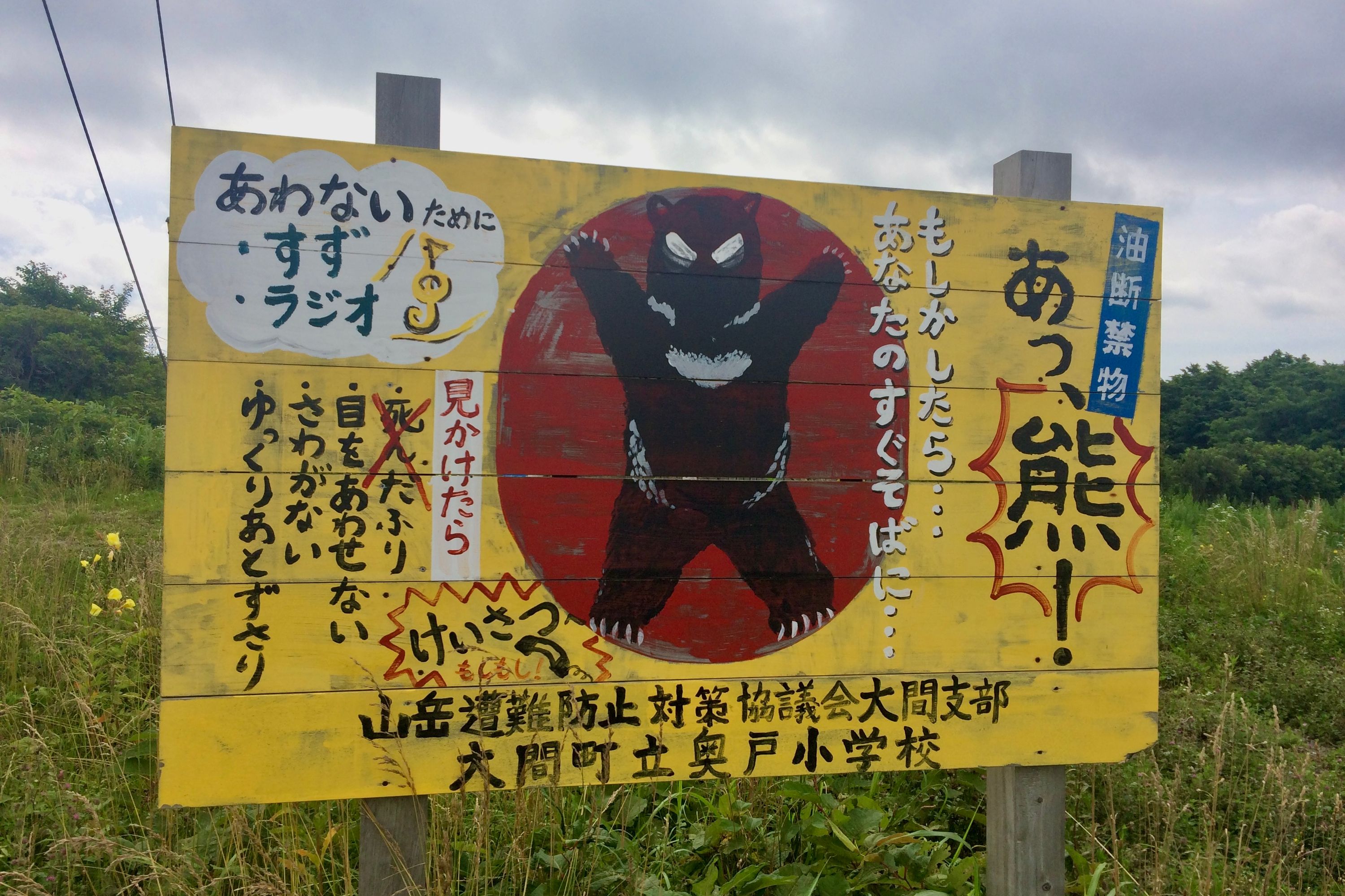 A black bear in a menacing pose on a red-on-yellow billboard with a lot of Japanese writing.