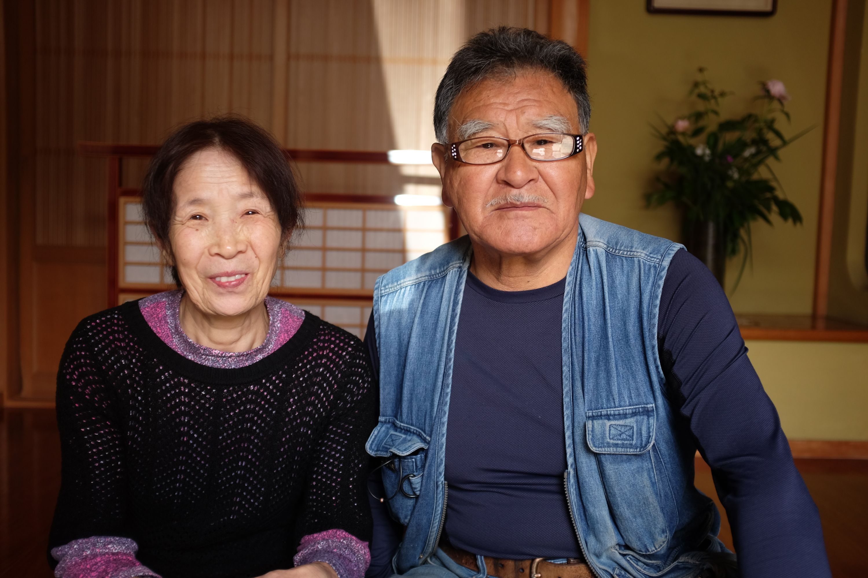 A Japanese couple pose for the camera in the entryway of their house.