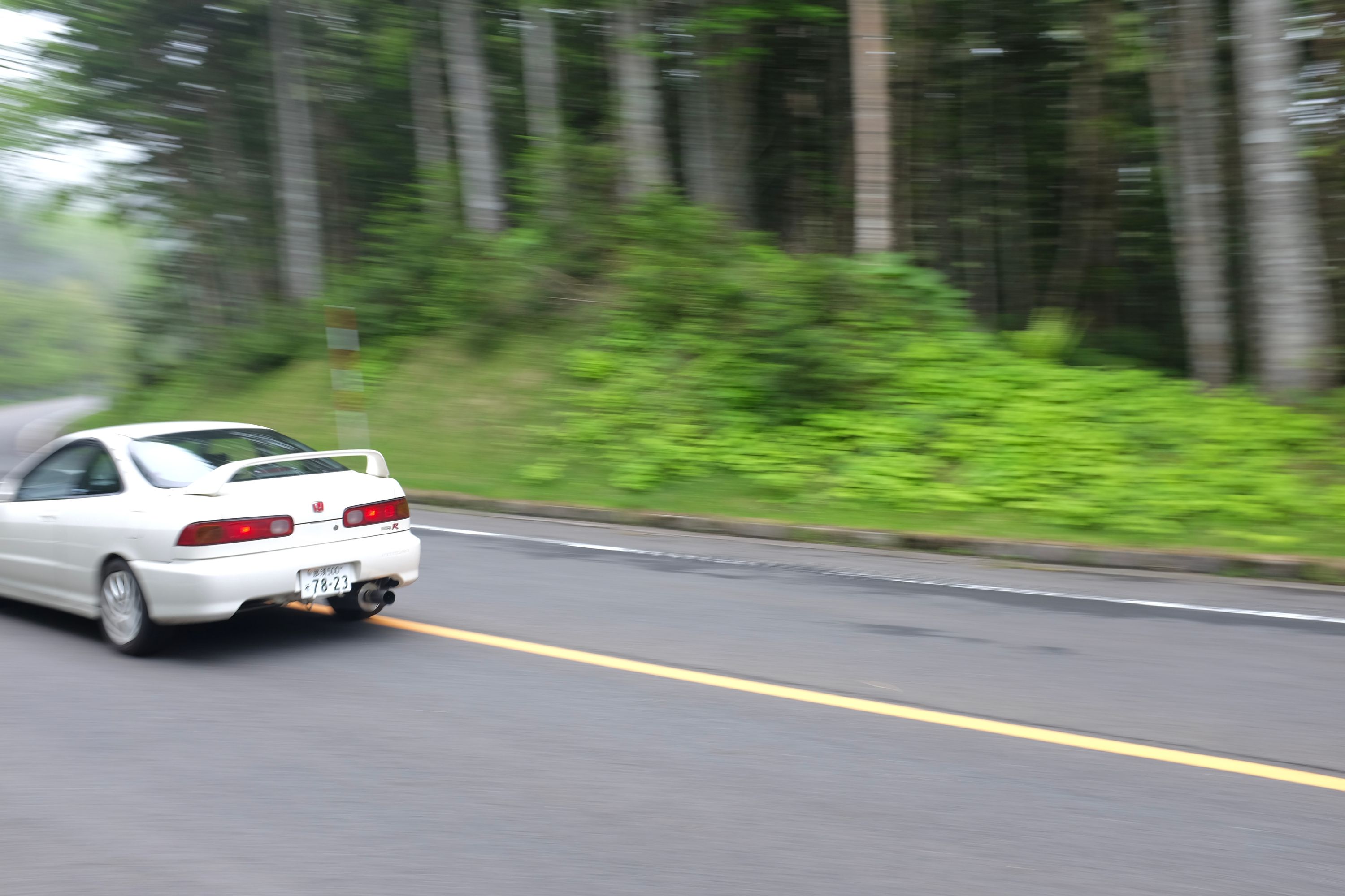 A white Honda Integra drives at high speed along a road in the forest.