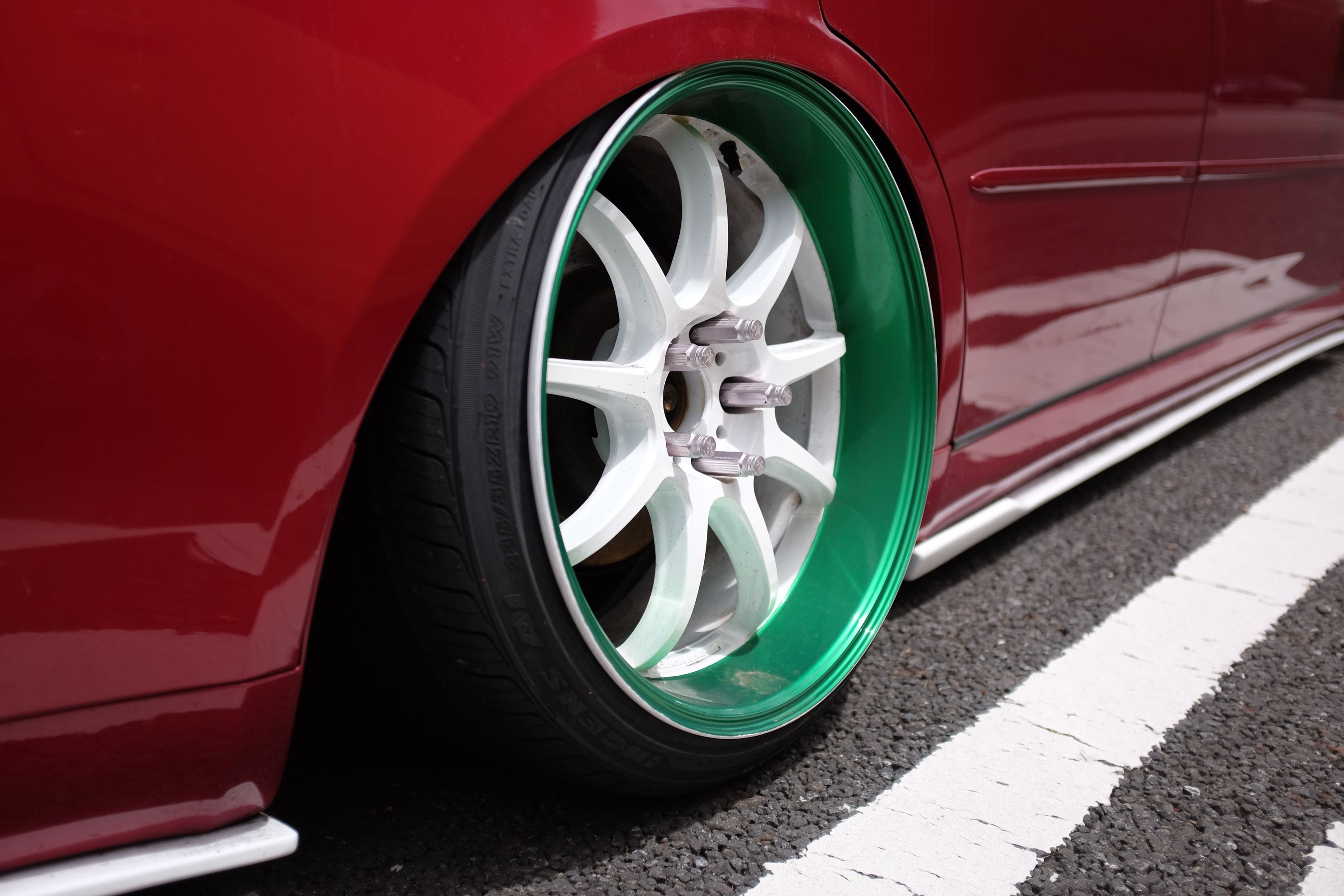 The white wheel of a red car which is lowered almost to the ground, a style called stanceworks.