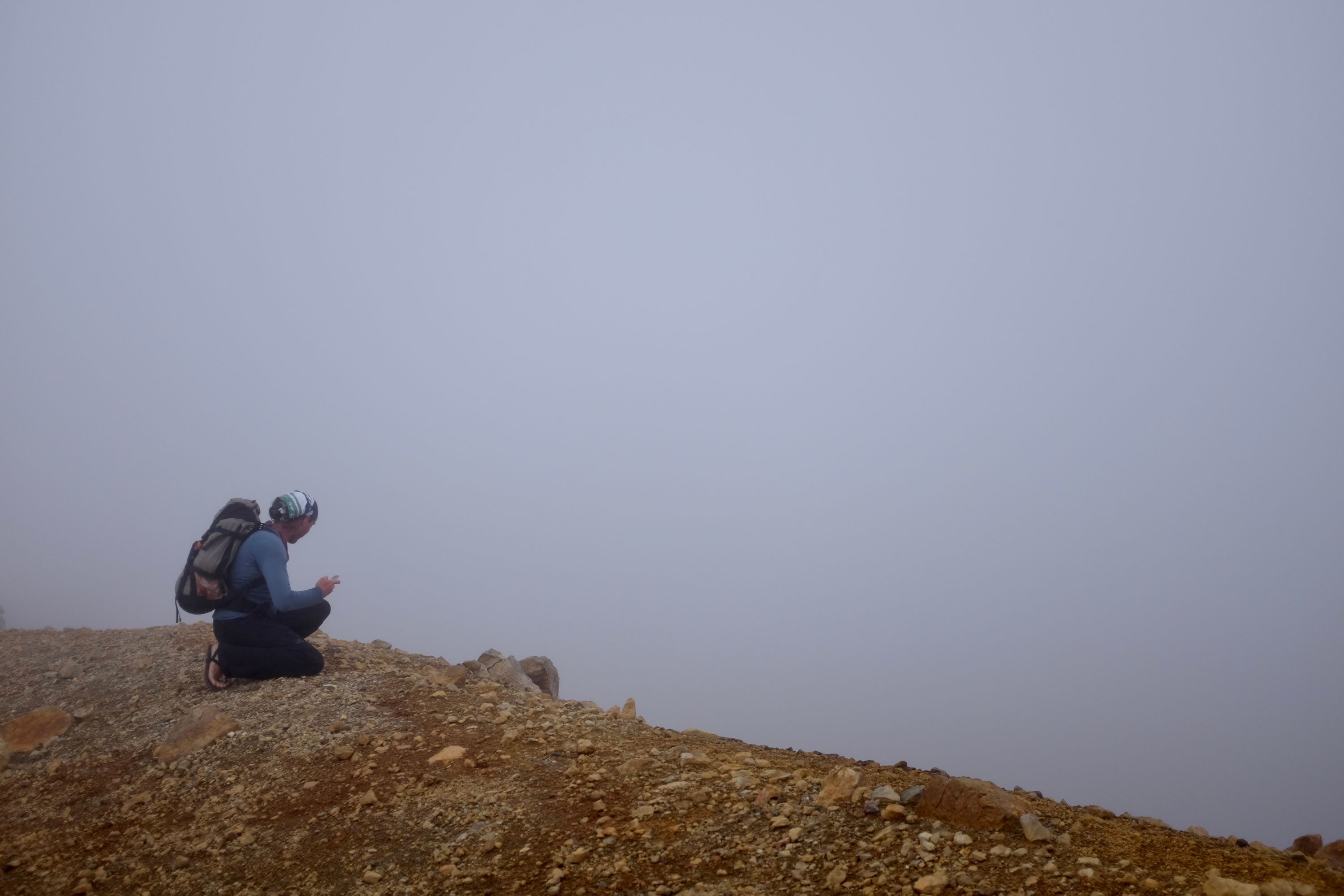 Gabor kneels at the edge of a crater, looking into a foggy void.