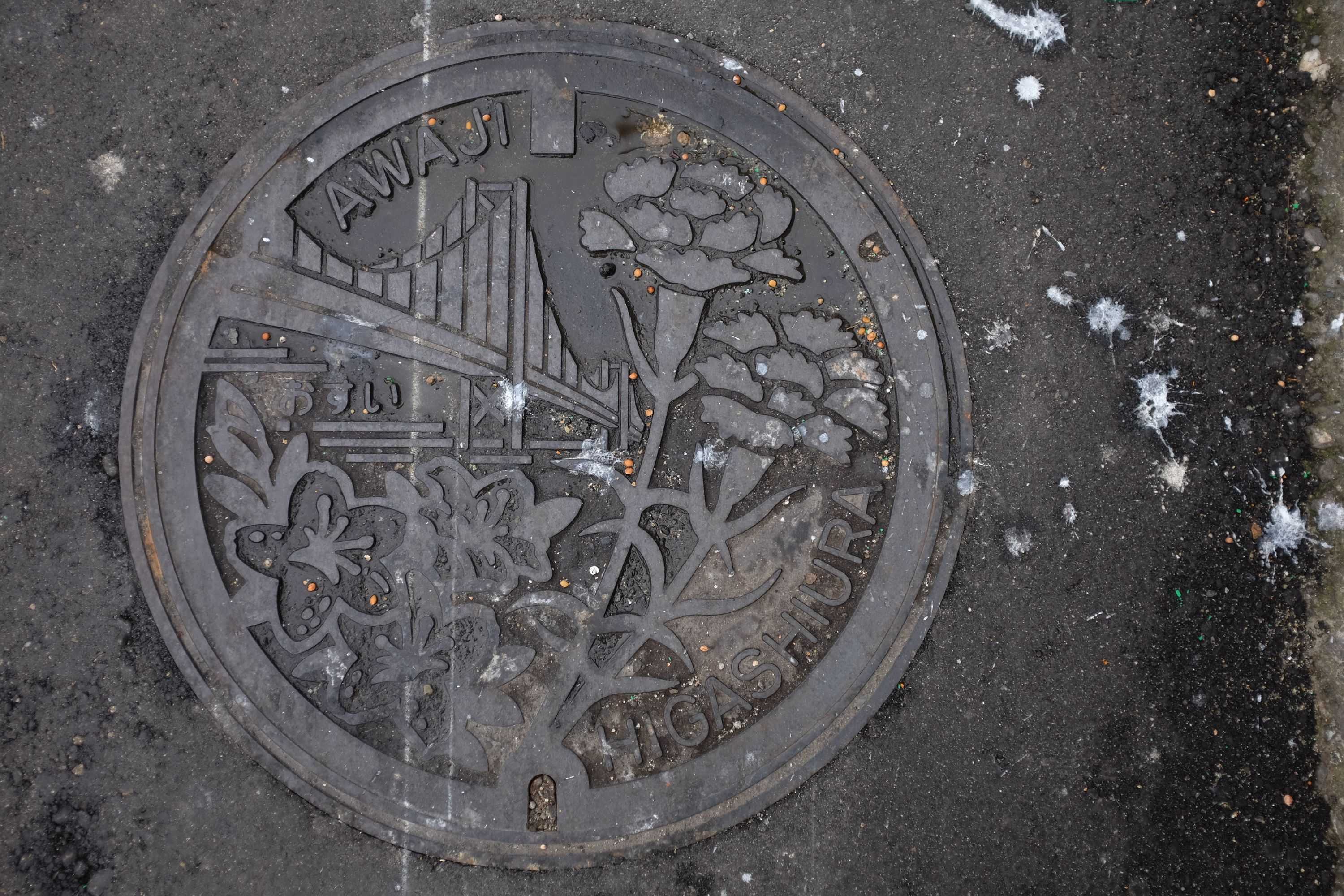 A manhole cover shows the Akashi Kaikyō Bridge and some flowers.