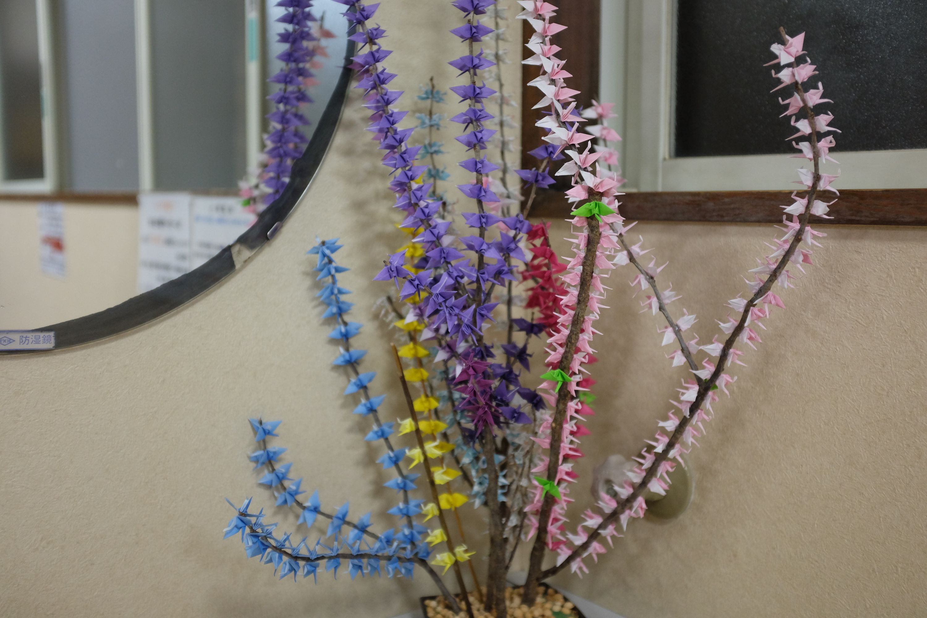 A flower arrangements in a bathroom has paper cranes in every color instead of flowers on the branches.