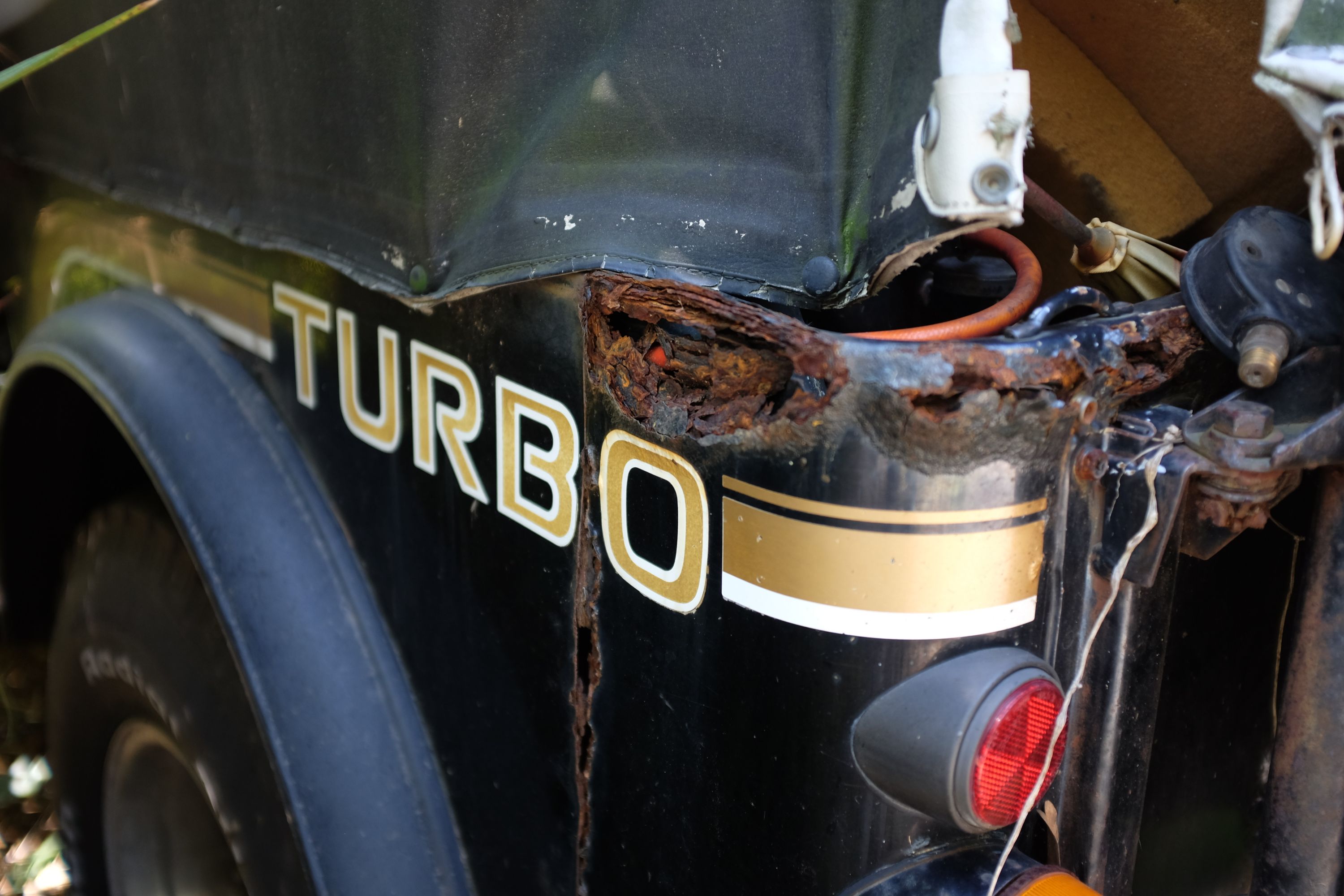 Detail of a rusty car with a sticker saying TURBO.