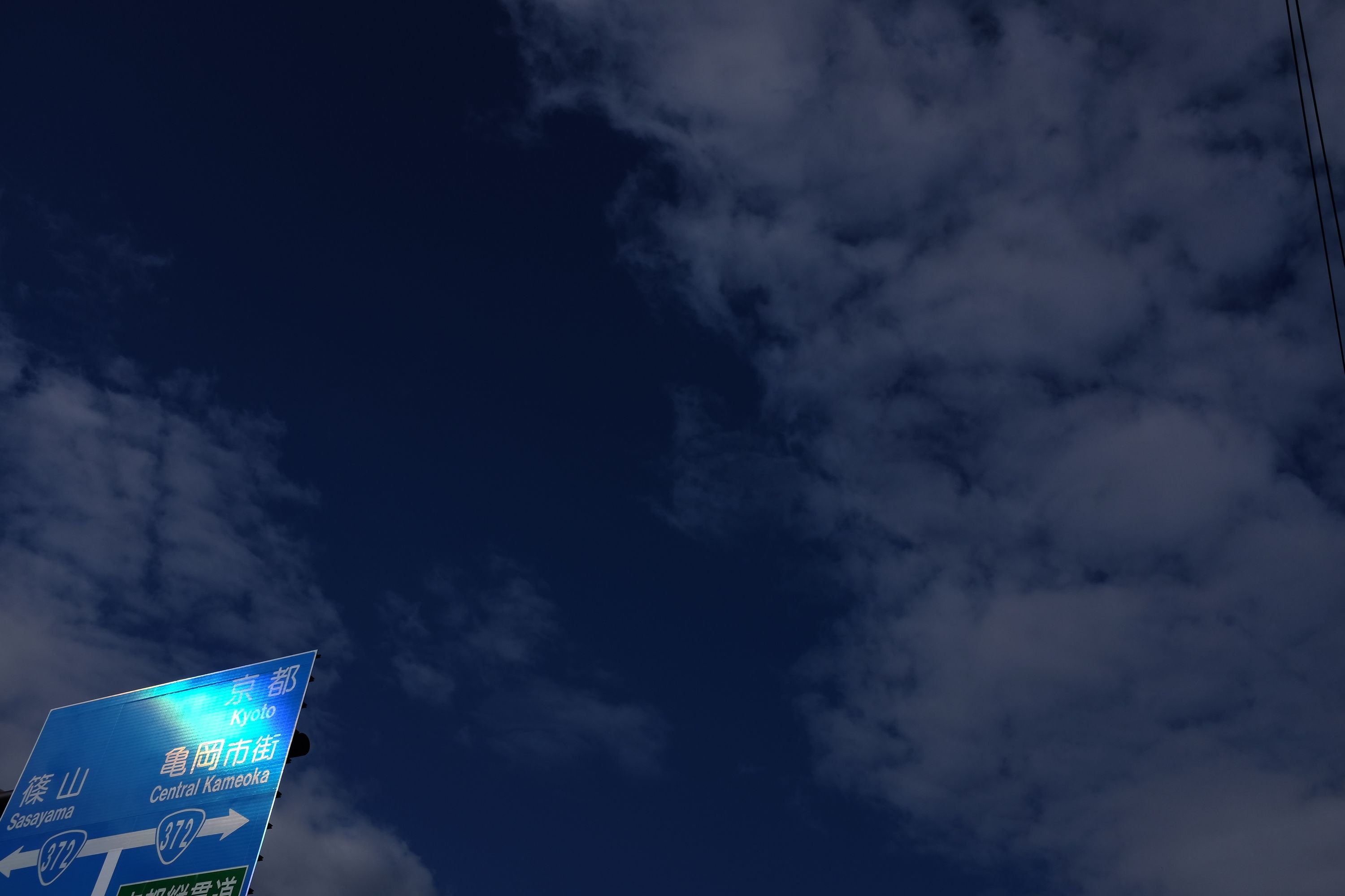 A road sign, in the lower left-hand corner of a picture shot against a deep blue, lightly clouded sky, shows the way to Central Kameoka.