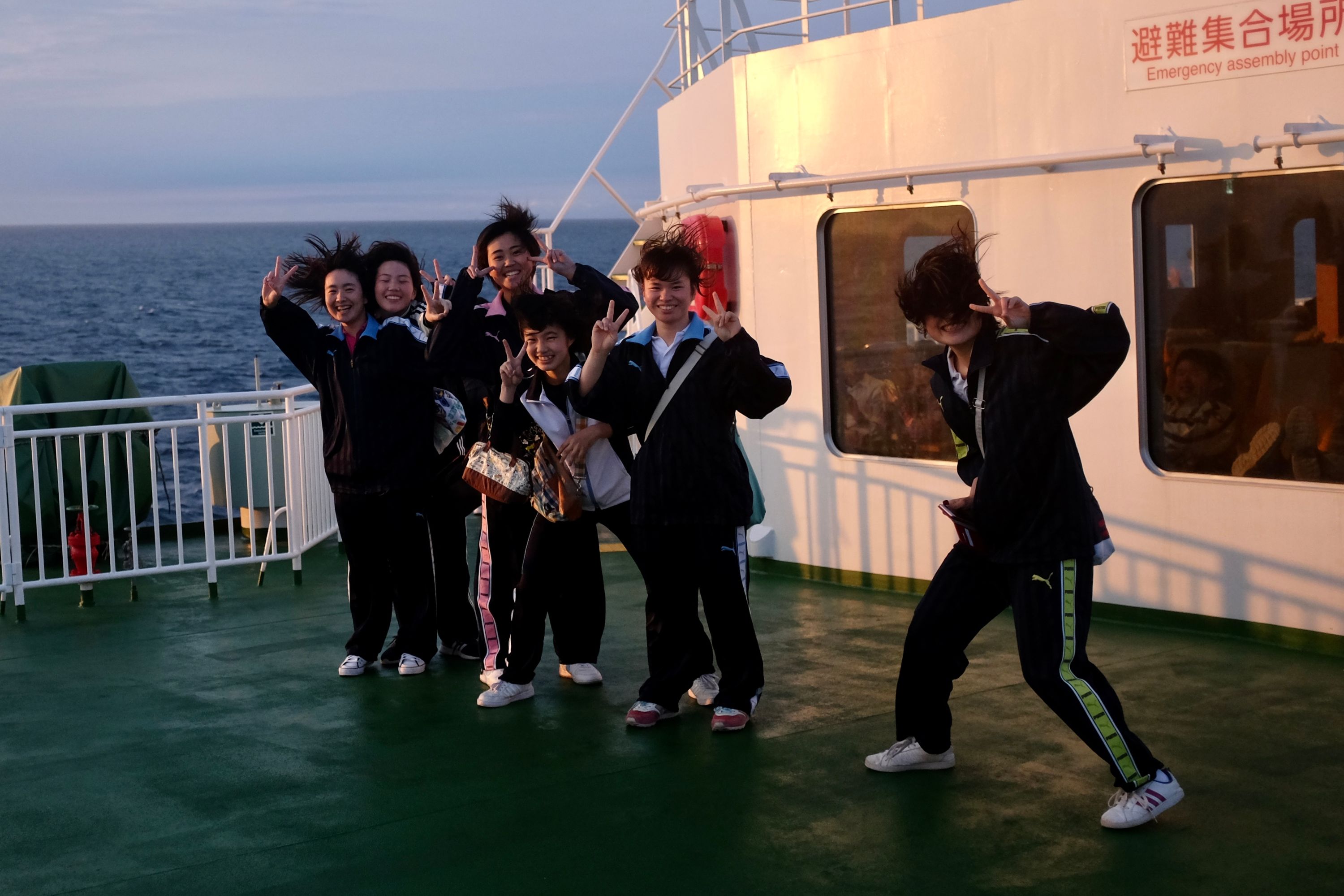 A group of girls on the same deck show V-signs into the camera, their hair tousled by what must be a very strong wind.