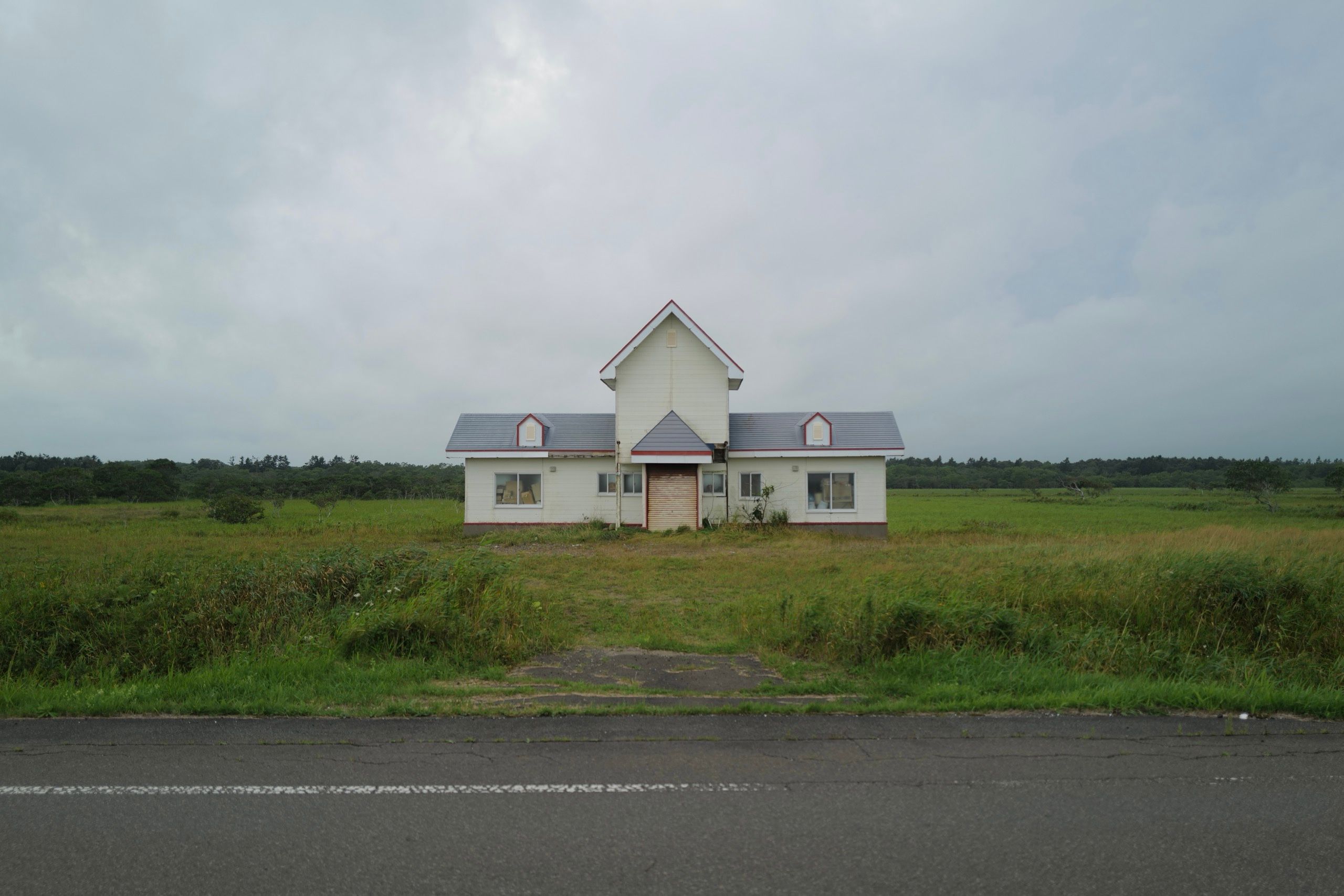 A European-looking abandoned buildings stands in a field off the road.
