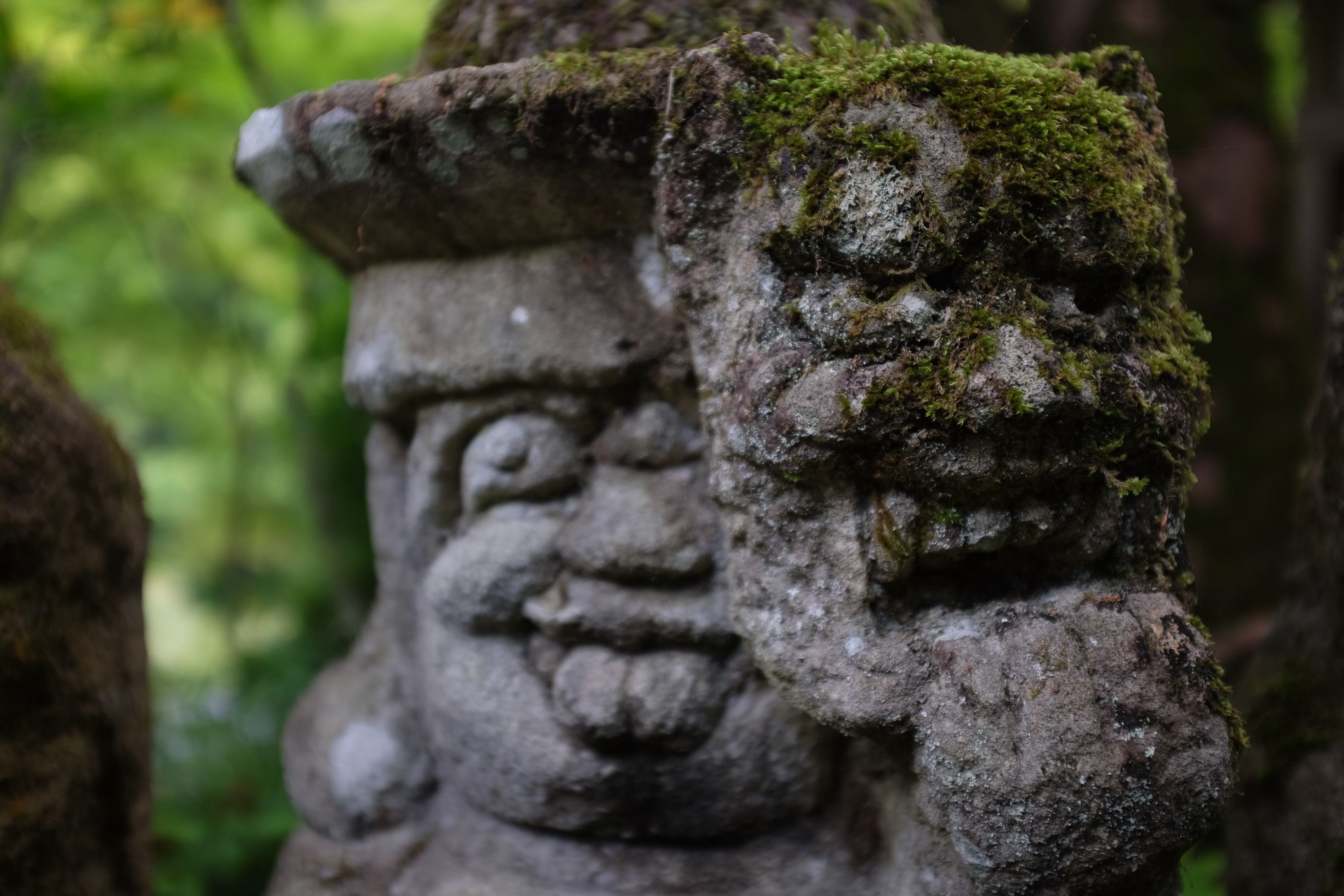 Two moss-covered stone statues of heads, one with bulging eyes and its tongue sticking out.