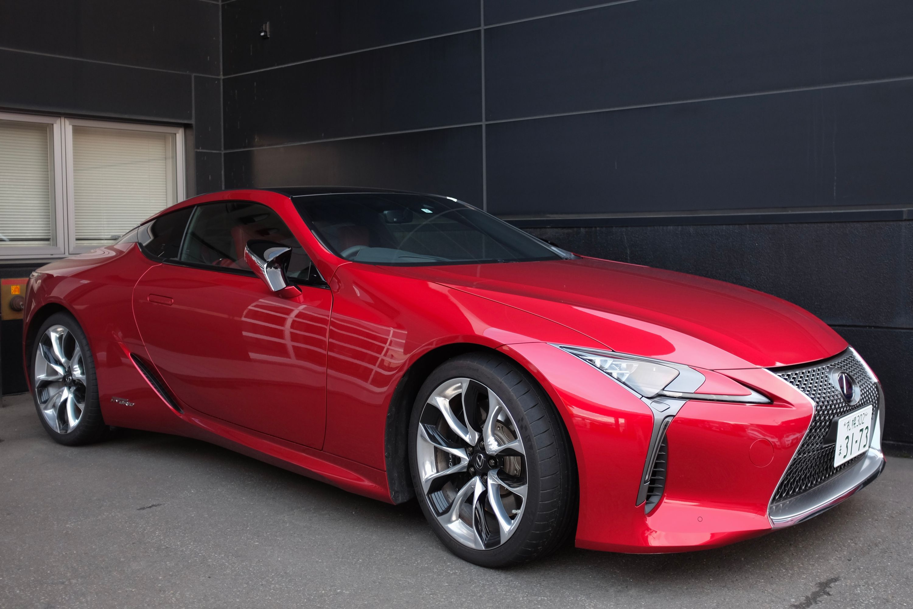 A red Lexus LC500H sports car parked by a dark grey wall.