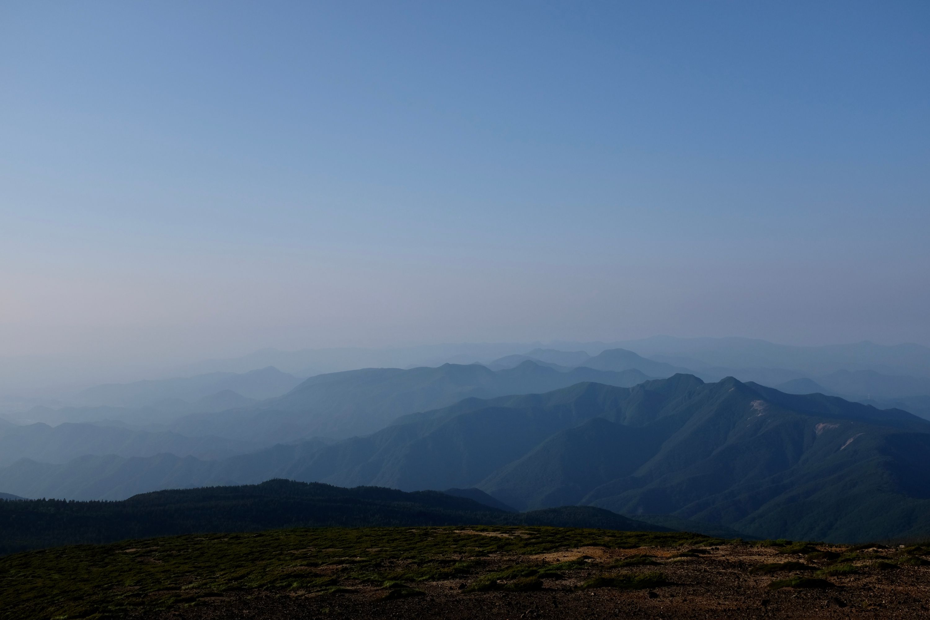 Ranges of low hills fade into the haze, as seen from a mountaintop.