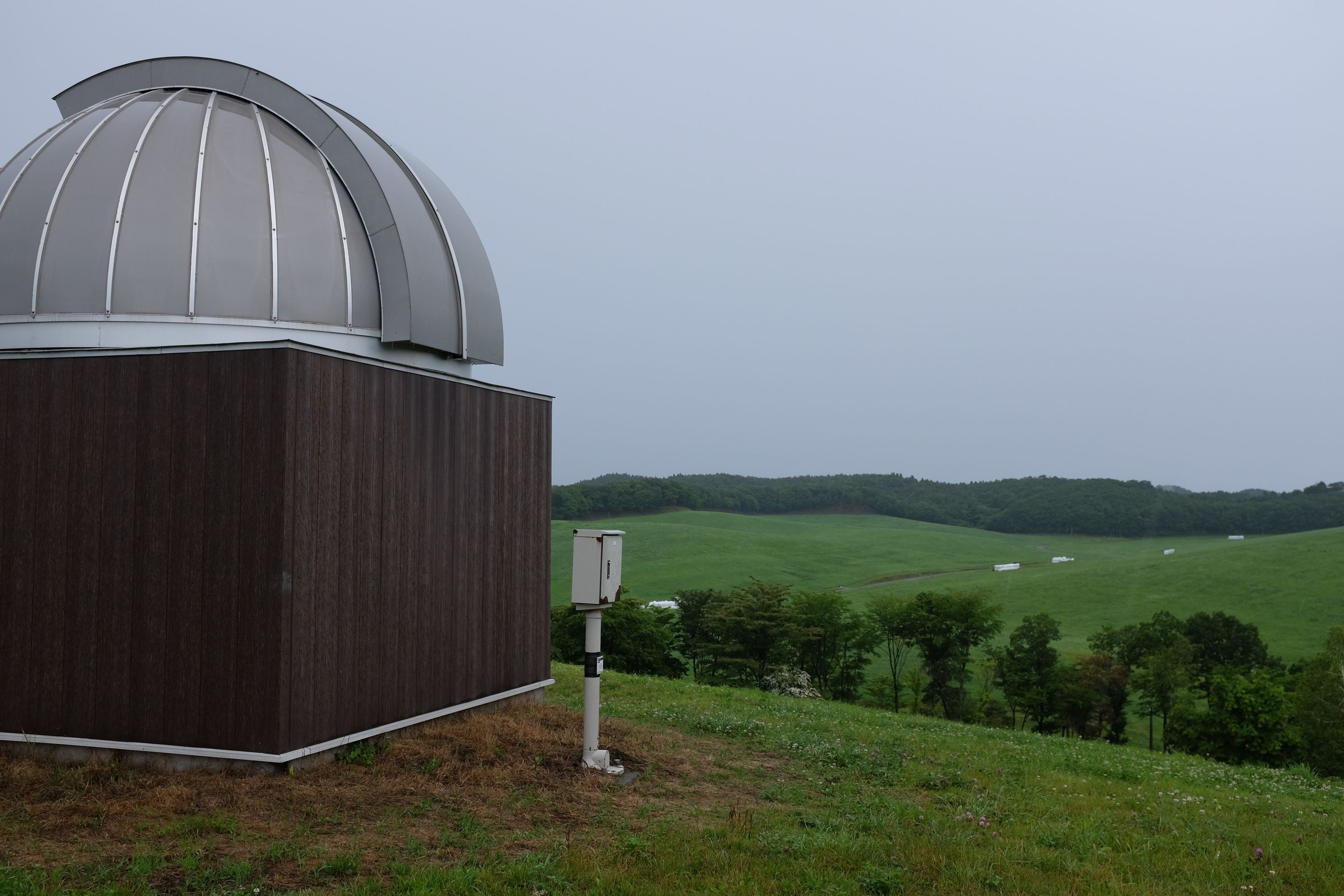 A small astronomical observatory over rolling green hills in the rain.