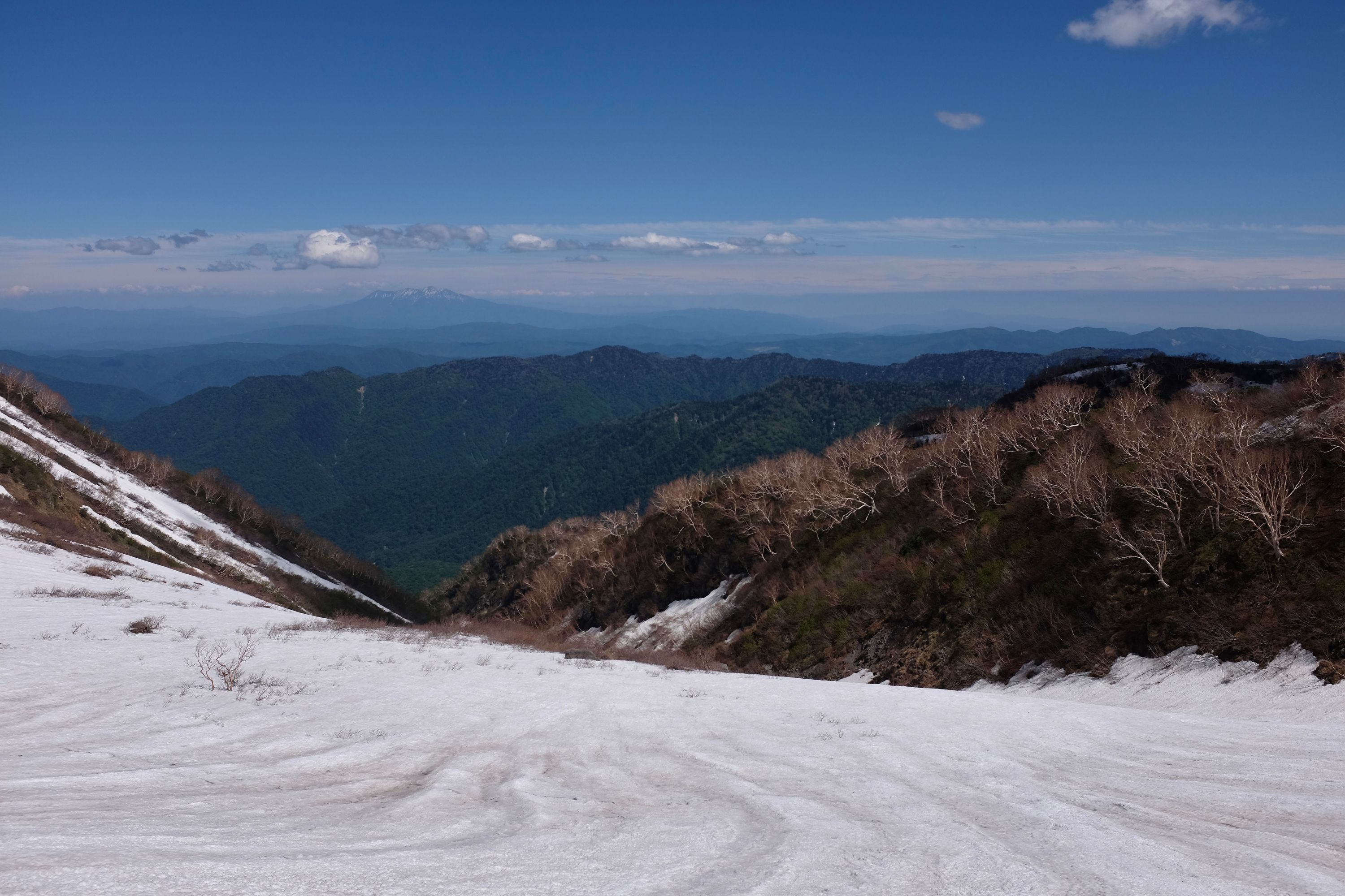 A steep snowfield leading down Hakusan, with Mount Ontake on the horizon.