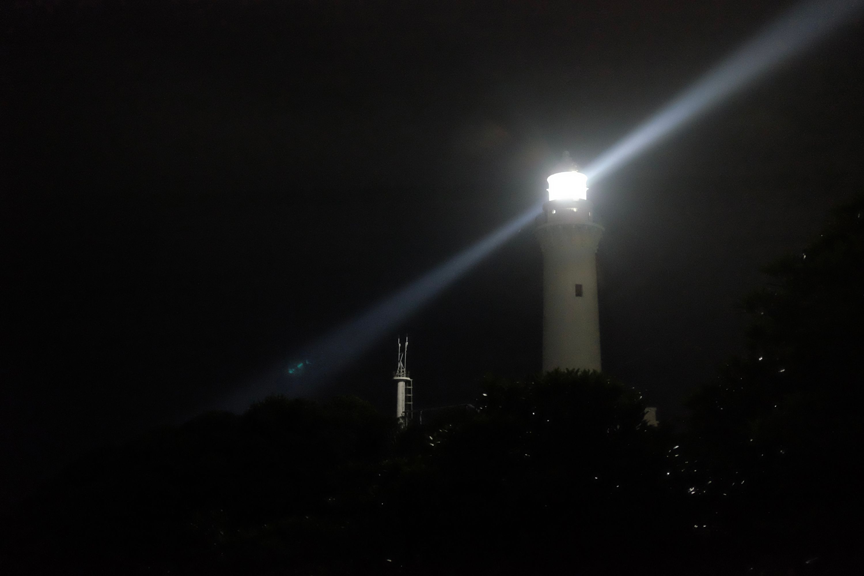 A lighthouse casts a beam of light in the night sky.