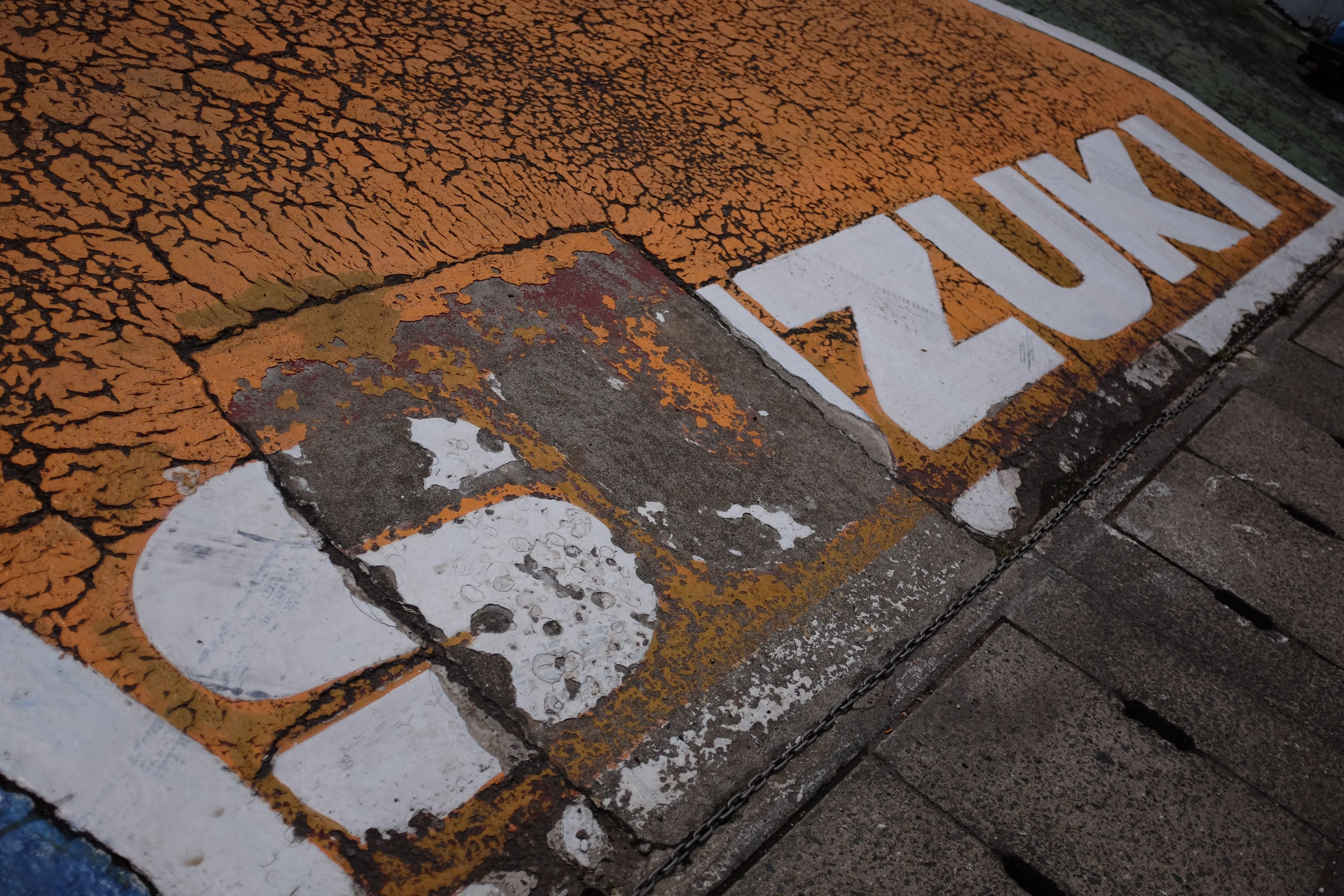 A faded yellow Suzuki sign painted on the ground.