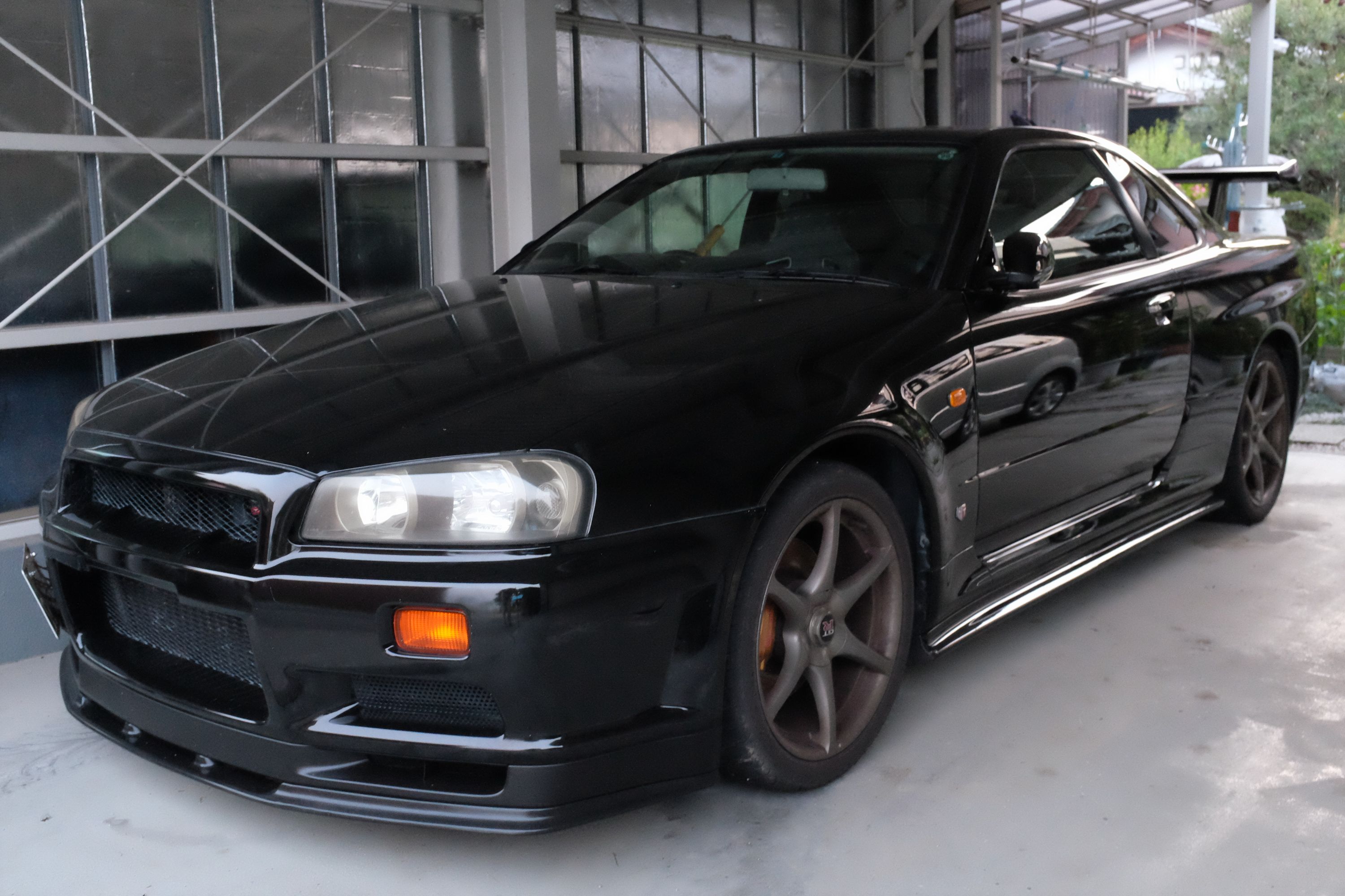 A menacing-looking black Nissan Skyline R34 with a big wing and custom bodywork.