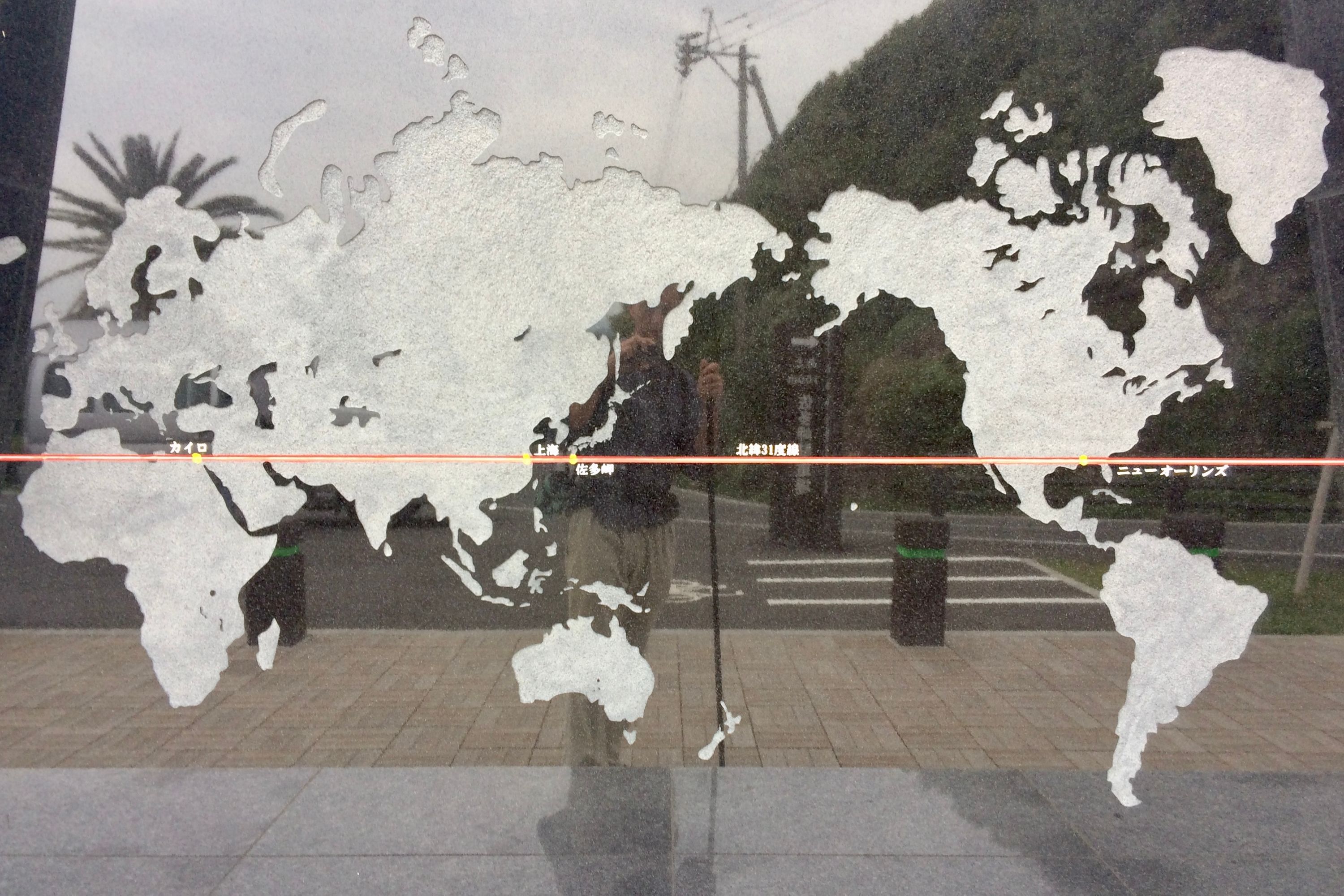 The author reflected in a memorial of the 31st parallel north, which shows a world map with the line running through it.