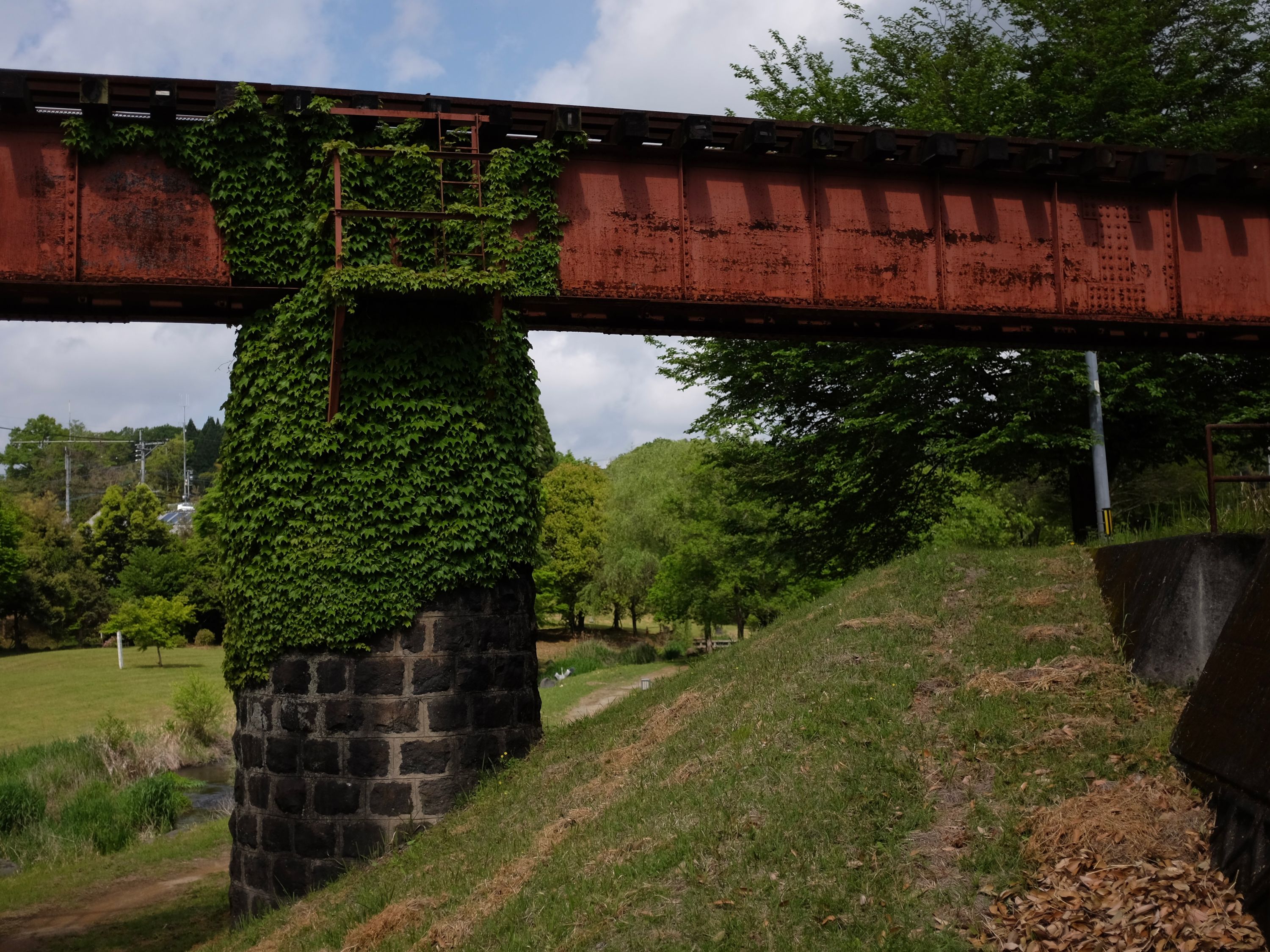 An old railway bridge of red steel and black basalt support columns.