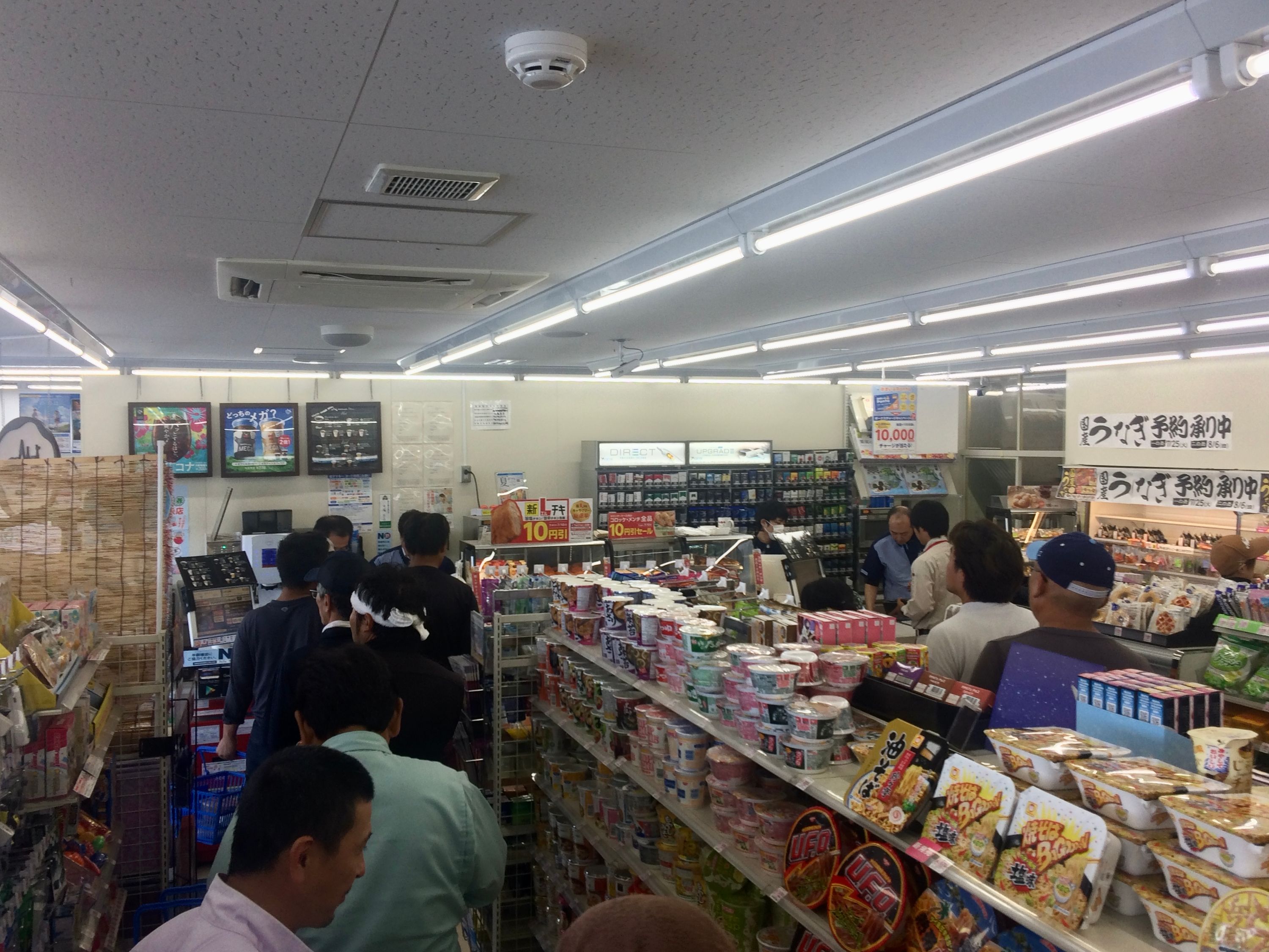 A long line of people wait in a convenience store.