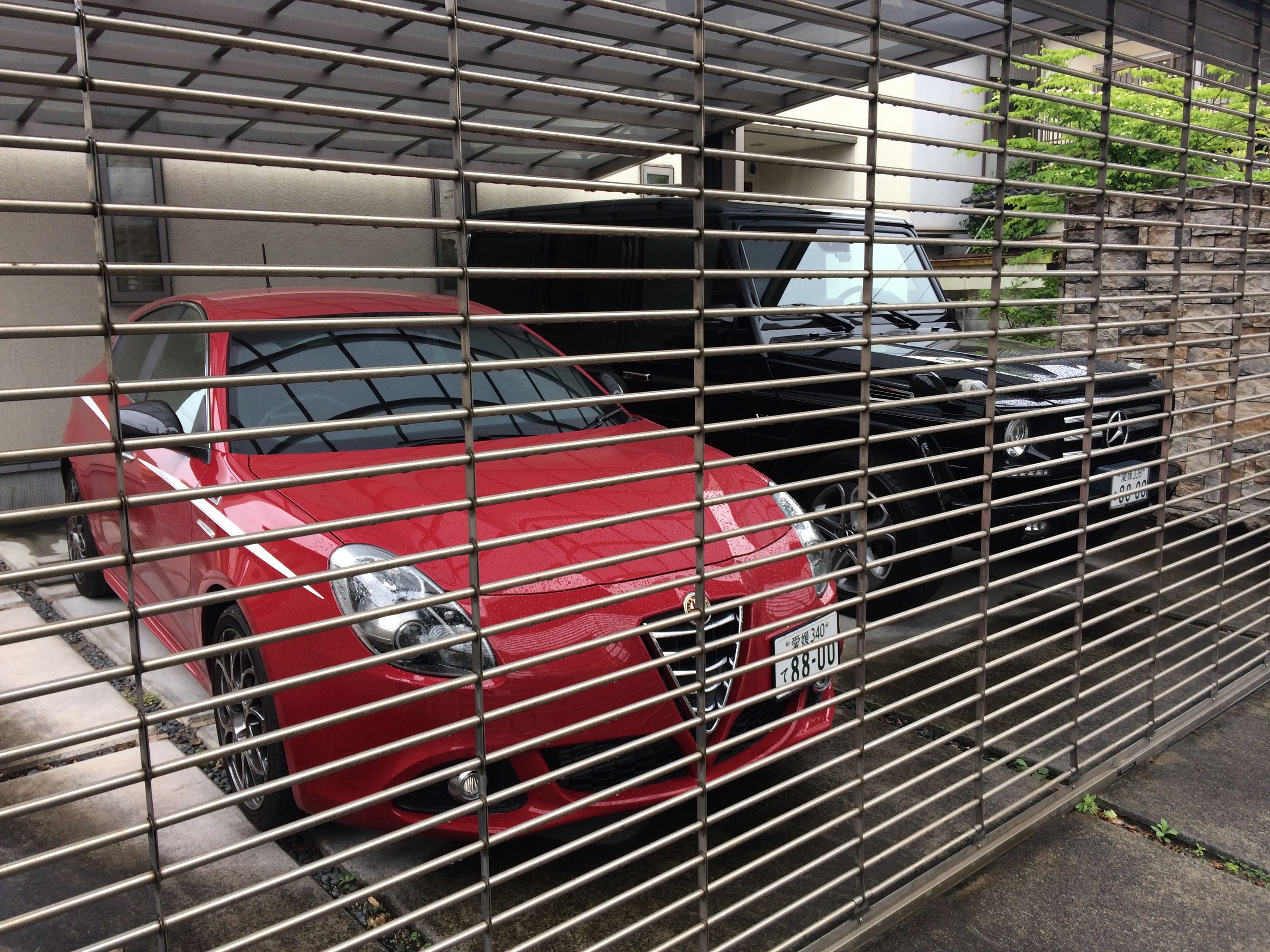 A red Alfa Romeo and a black Mercedes-Benz G-Wagen parked in a driveway behind a grate.