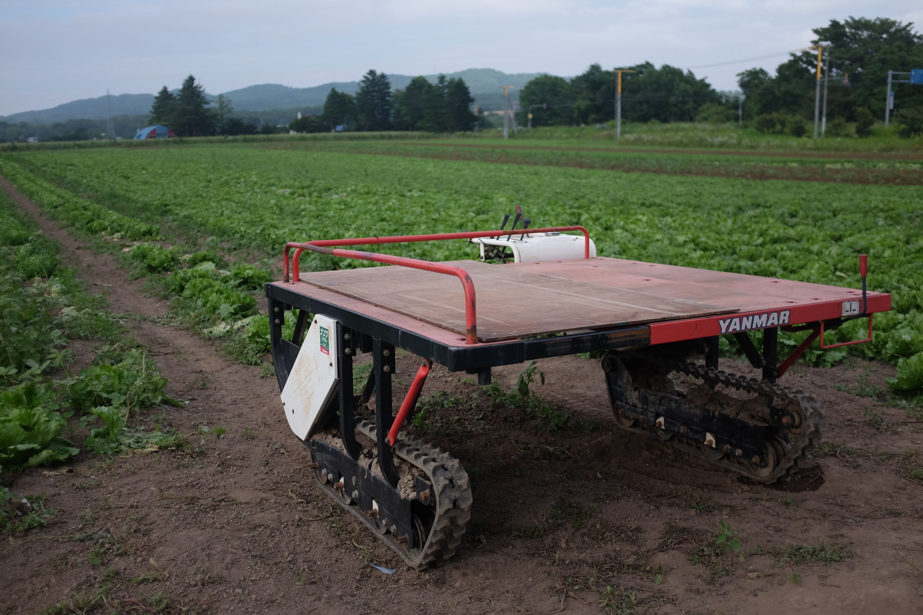 A small, tracked planter parked by a green field.