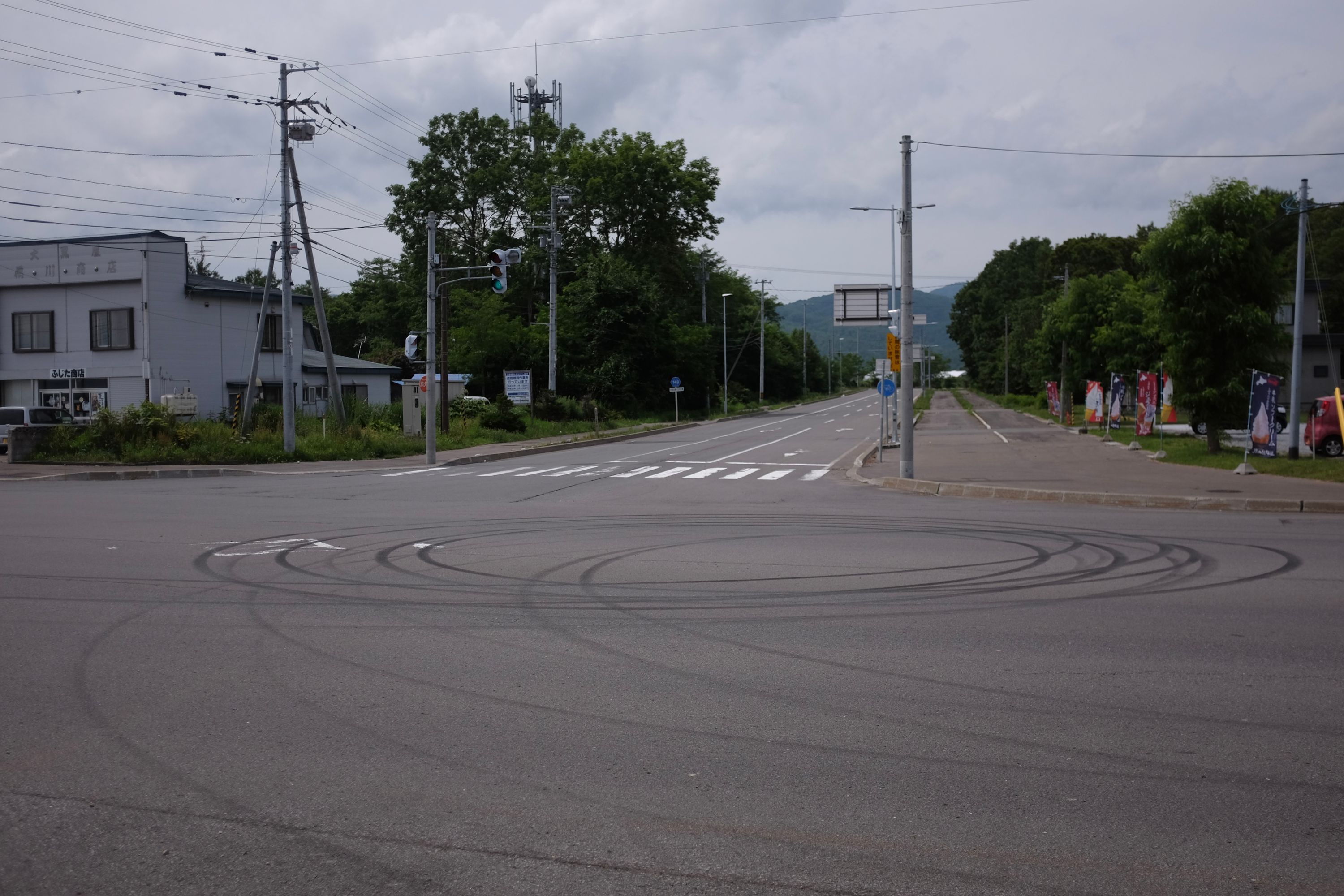 An empty street corner in a small town with marks on the asphalt indicating someone having done donuts.