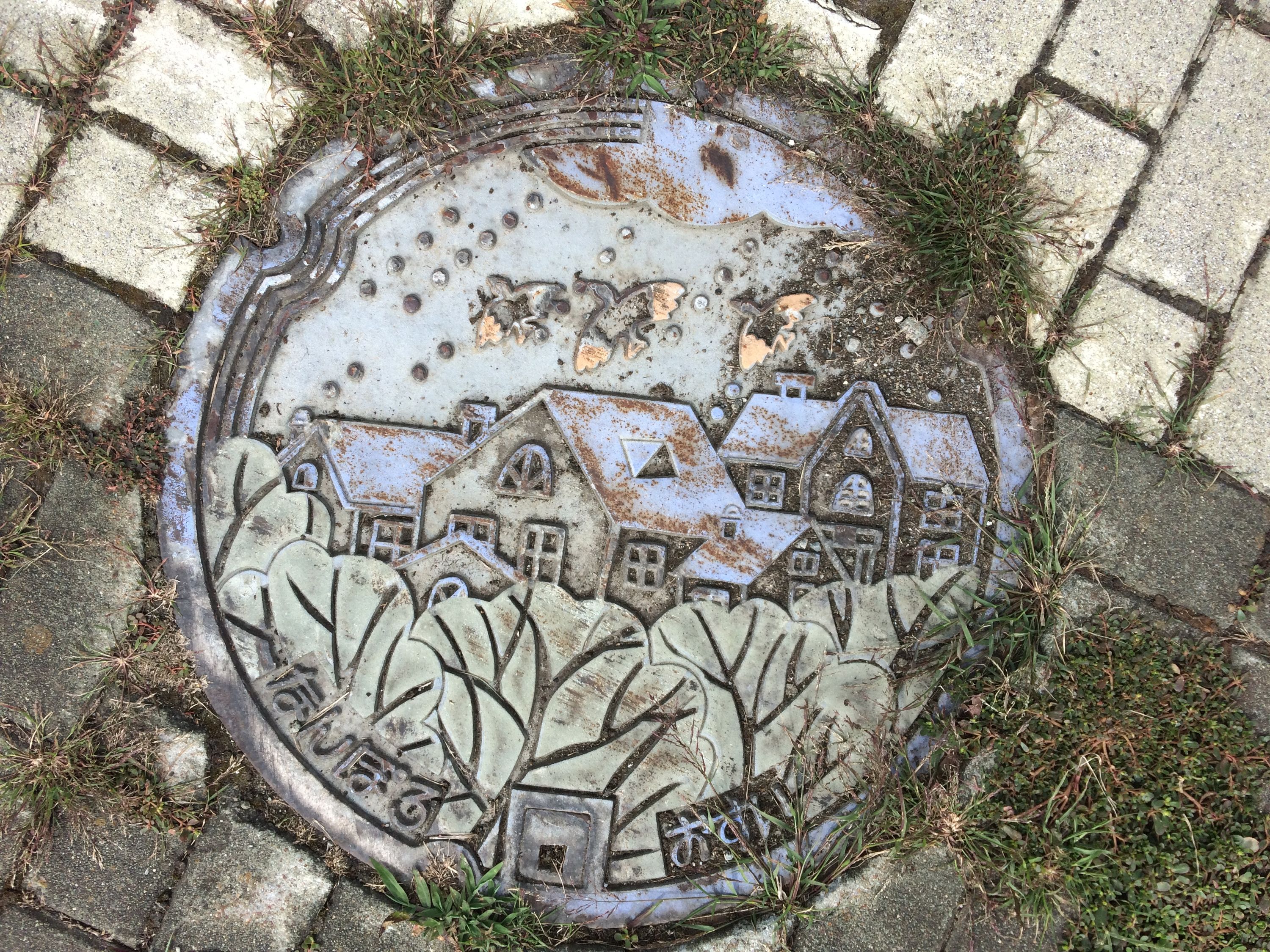 Manhole cover with trees, houses, and birds.