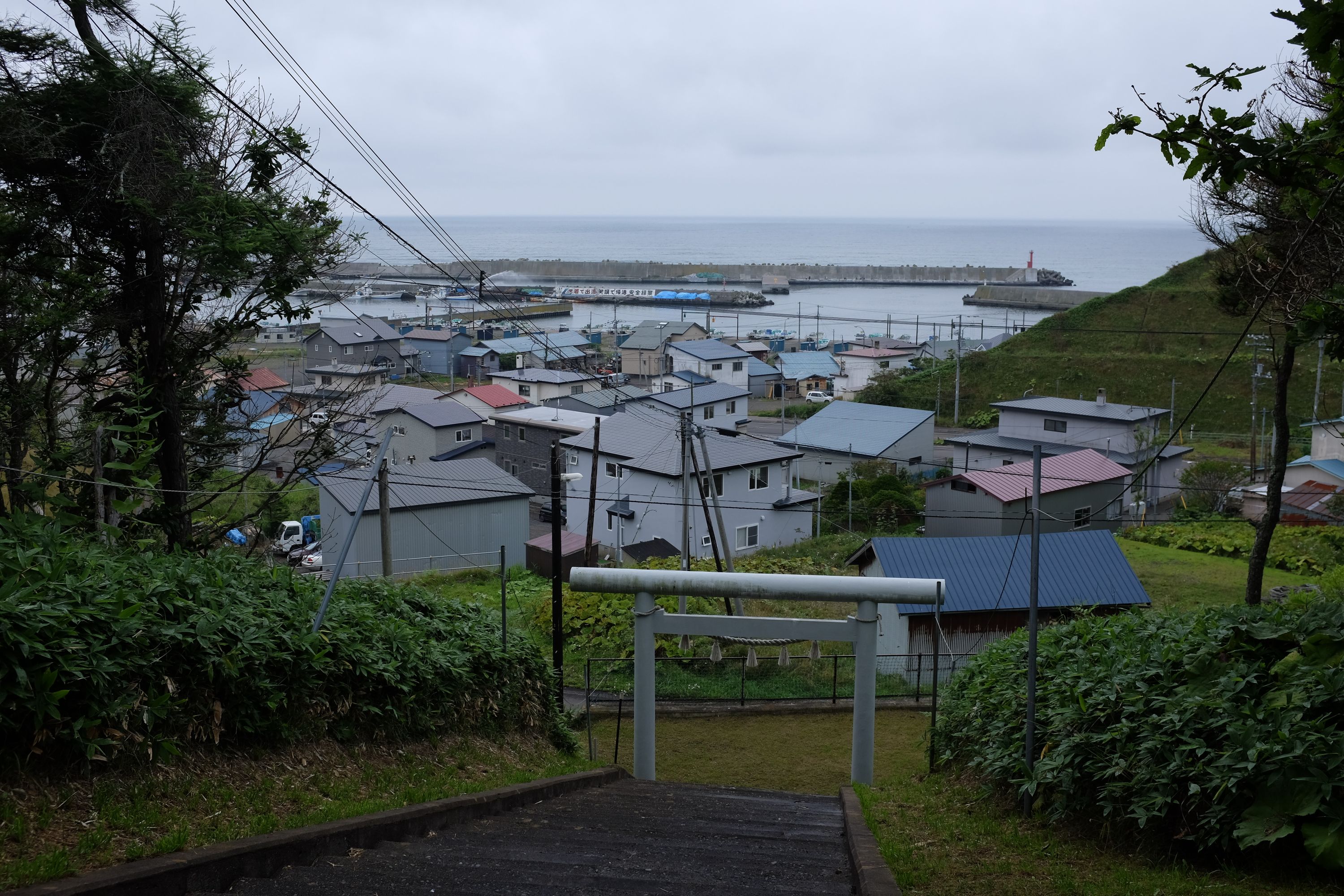 View above a shrine gate of a Japanese fishing village under a grey sky.