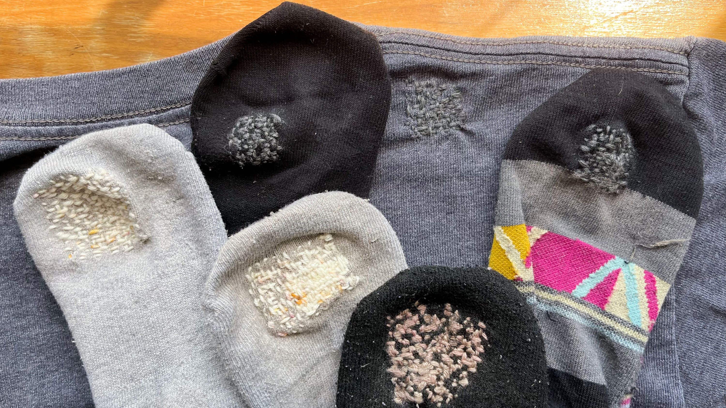 A collection of socks and t-shirts with small mends/reinforcing stitches.